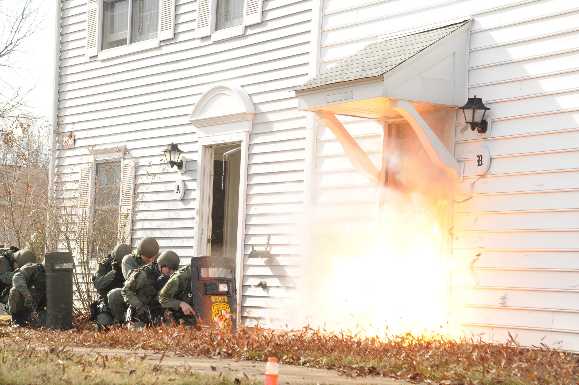 Members of the Maryland State Police Special Tactical Assault Team Element conduct a training exercise with 316th Security Forces Squadron members Jan. 19, 2010, to demonstrate protocol procedures for entering a building with potentially armed hostiles. The joint exercise, held in unusable base housing, is a means for the the 316 SFS and MDSP forces to pool experience, materials and other training techniques. The doorway explosion is the result of a simulated forced entry in the event armed inhabitants refused police access. The charge that removed the door and caused it to travel a few feet consisted of 100-grain detonation cord.