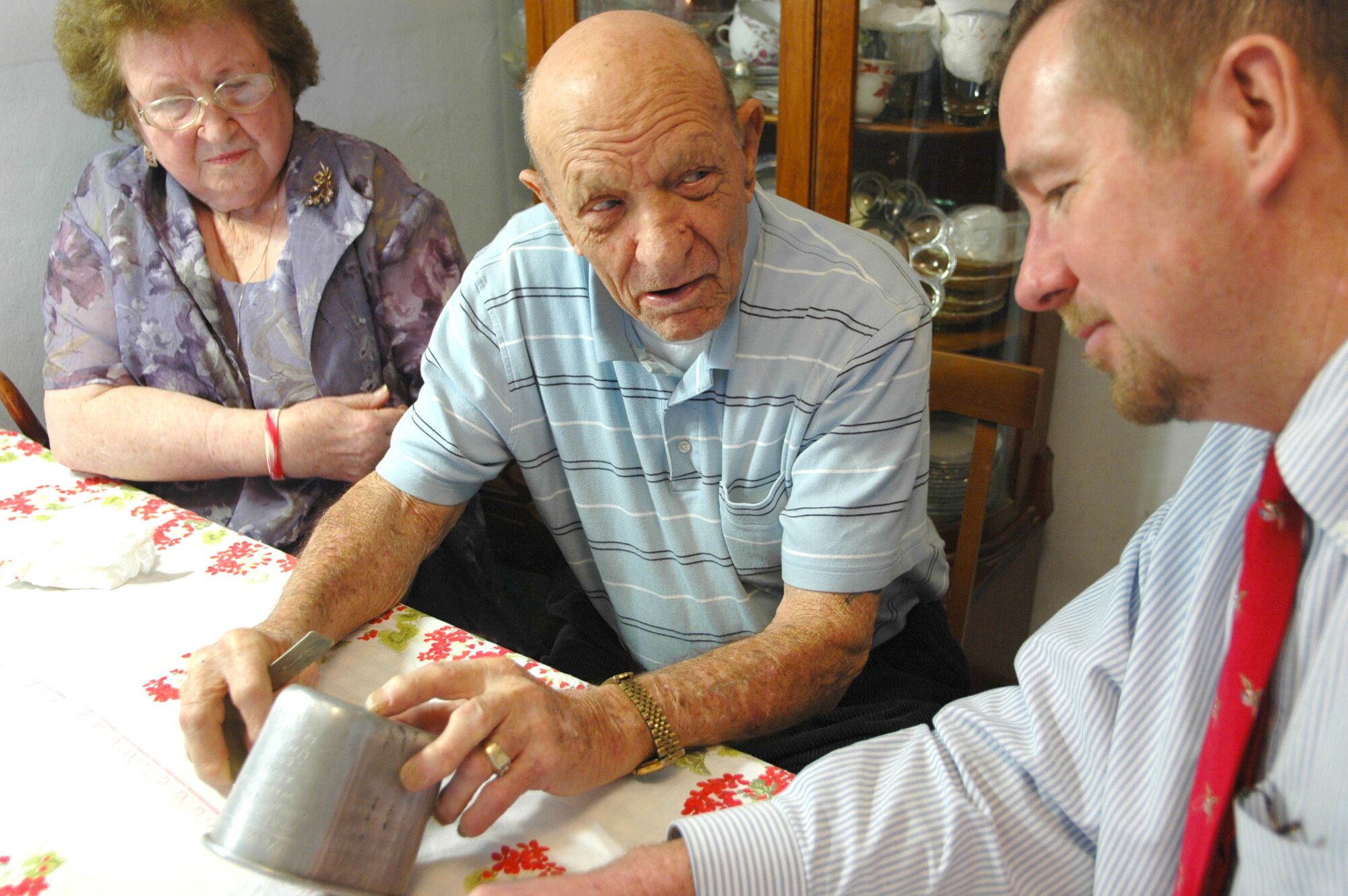 Robert Freese, center, tells James Bement the story behind the etchings in his canteen cup. During World War II, Mr. Freese etched the names of all the places he saw during his combat tour. Mr. Bement recently wrote a book from the perspective of the 93-year-old veteran and his wife, Leona, drawing on their wartime correspondence.(Air Force photo by Howdy Stout)
