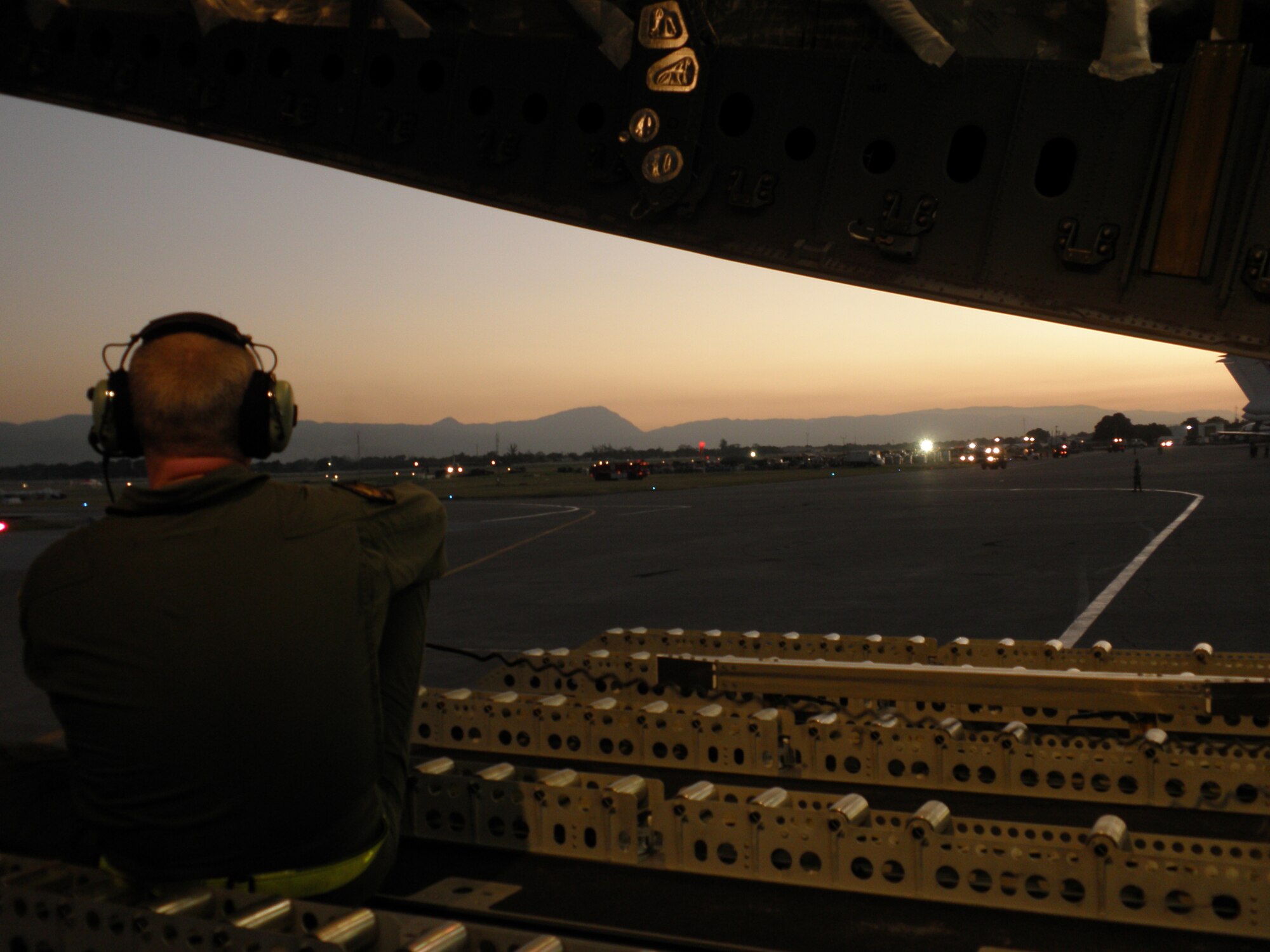 Norwegian Air Force 1st Lt. Jan Barre Prestbakmo, a loadmaster for the Heavy Airlift Wing out of Papa Air Base, Hungary, gives directions to the pilot as his C-17 transport aircraft backs up in preparation for takeoff from the main airport at Port-au-Prince, Haiti, Jan. 18.  The aircraft and multi-national aircrew had just delivered 15 pallets of material to construct a headquarters for aid workers at the airport. The air relief is being delivered in response to a massive earthquake that struck Haiti Jan. 12. This is the first humanitarian assistance operation flown by the Heavy Airlift Wing since it stood up in July 2009.  The wing is a multi-national force made up of Airmen from 12 nations.   (U.S. Air Force photo by Technical Sgt. Richelle Morey)           