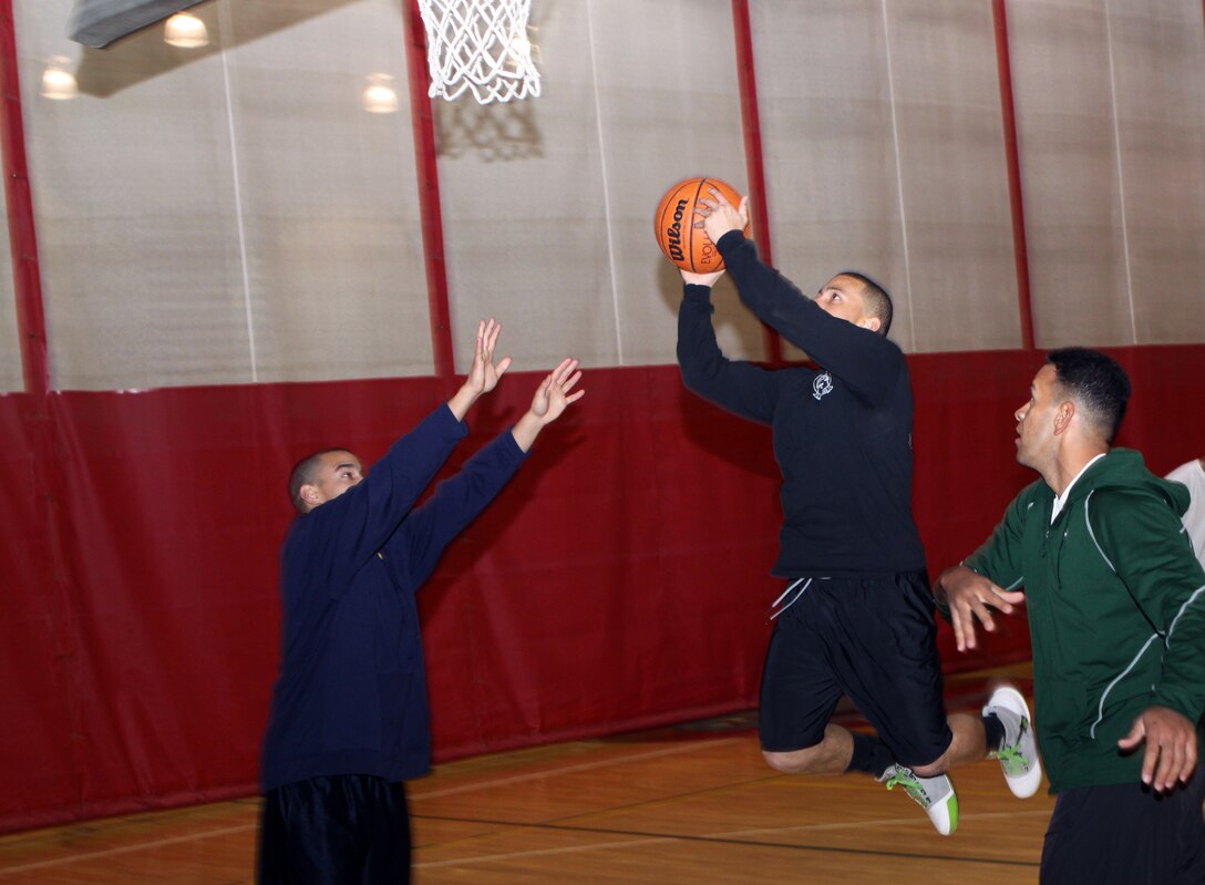 Ernesto Raya, aviation information systems specialist, Medium Light Attack Helicopter Squadron 369, 3rd Marine Aircraft Wing, jumps to score a slamdunk from his opposing players Ariel Garcia, administration clerk, Marine Medium Helicopter Training Squadron 164, 3rd MAW, left, and George Moleni, maintenance management specialist, 1st Battalion, 11th Marines, 1st Marine Expeditionary Force, during a three-man practice game at the Back in the Saddle Sports Jam Sereis event Jan. 22. The Back in the Saddle Event is one of the Sports Jam Series events that promotes physical activity and offers a free, safe and alcohol-free alternative for service members and their families.