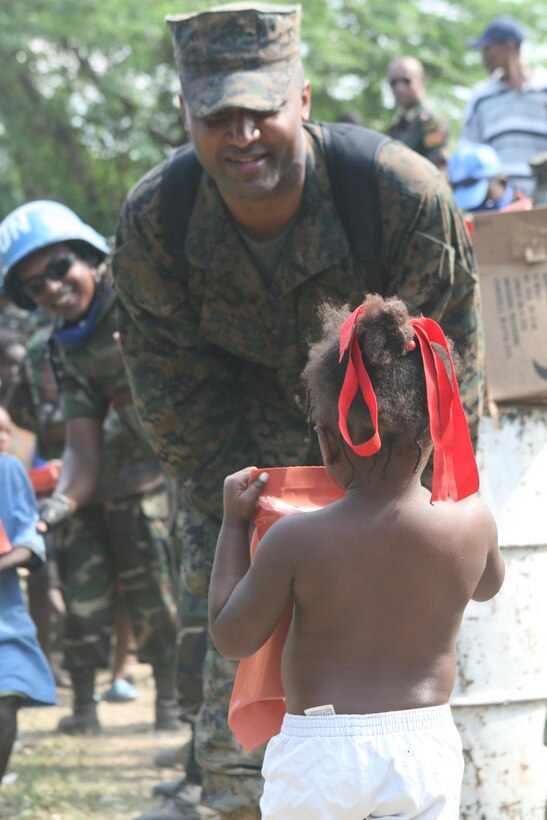 Staff Sgt. David Charlton, Logistics Chief, Security Cooperation Marine Air Ground Task Force, Africa Partnership Station 10, hands out food to an young Haitian girl.  More than 5,000 Haitians have lined up at multiple distribution sites to receive food and water offered by Marines and Sailors from the SCMAGTF as they teamed up with Sri Lankan UN workers to help pass out over 10,000 Meals, Ready-to-Eat, Jan. 24 through 29.