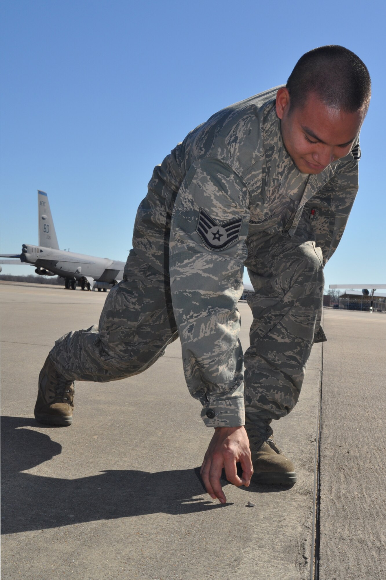 Staff Sgt. Christian Inguillo, a Regular Air Force electronic warfare attached to the 917th Aircraft Maintenance Squadron on Barksdale Air Force Base, La., removes a rock from the flight line during a foreign object damage (FOD) walk on Barksdale Jan. 22, 2010. The 917th AMXS, made up of both 917th personnel and Regular Air Force members attached to the unit, conducts a FOD walk every Friday, collecting any type of FOD in order to minimize the chances of damage to aircraft on base. . Rocks, such as this one, broken pavement or garbage are all considered to be FOD. (U.S. Air Force Photo/Senior Airman Crystal Marie Jordan)