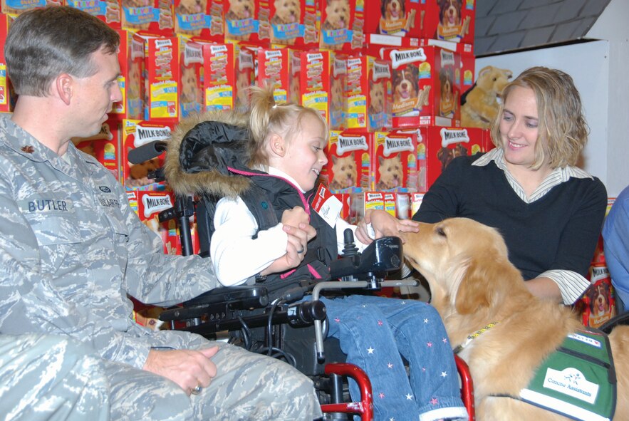 Ten-year-old Alexis Butler greets a “K-9 assistant” Friday at the Maxwell Commissary. The Golden Retriever is similar to the one she will receive this summer to help her cope with cerebral palsy. Alexis is flanked by her parents, Maj. Todd Butler of the Air Command and Staff College faculty and Maj. Sara Butler, commander of the reserve 908th Military Support Flight.(Air Force Photo by Bennett Rock)