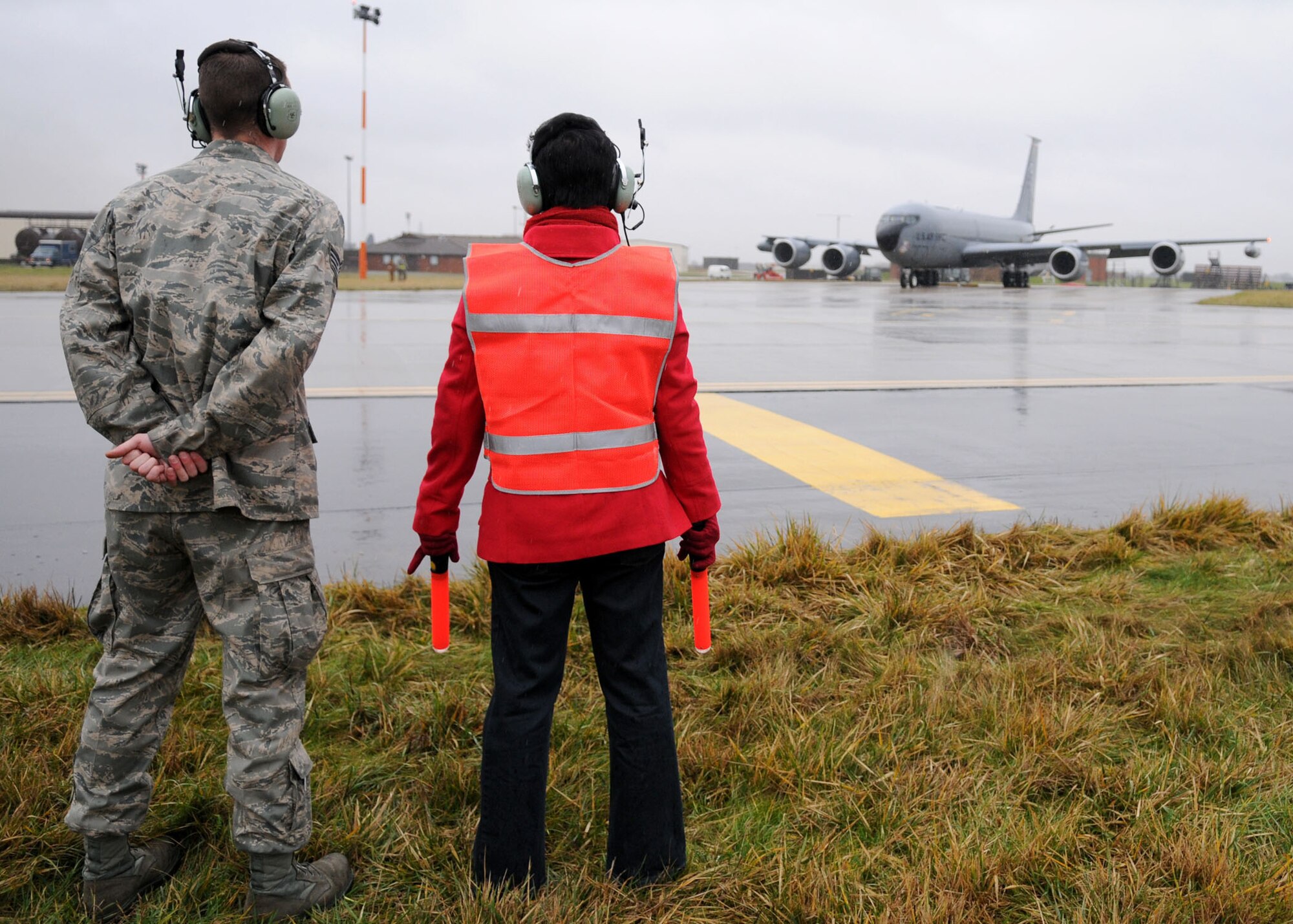 Karen Abeyasekere, right, 100th Air Refueling Wing Public Affairs, waits for the signal of flashing lights from Capt. Clint Albaugh,aircraft commander, and  Capt. Chris Saettel, co-pilot, (both from the 351st Air Refueling Squadron) aboard a KC-135 Stratotanker, Jan. 22, 2010. The event was part of a series of stories in which Ms. Abeyasekere experiences Air Force tasks first hand, and then writes about them for the base public Web site. This particular story focused on crew chiefs and marshaling aircraft. Staff Sgt. Glenn Hendrix, left, 100th Aircraft Maintenance Squadron, stands close by to offer assistance and ensure the correct marshaling signals are given so the aircraft can take off safely. Sergeant Hendrix, a crew chief, regularly marshals base aircraft, which is one of the many aspects of his job. (U.S. Air Force photo by Staff Sgt. Jerry Fleshman)