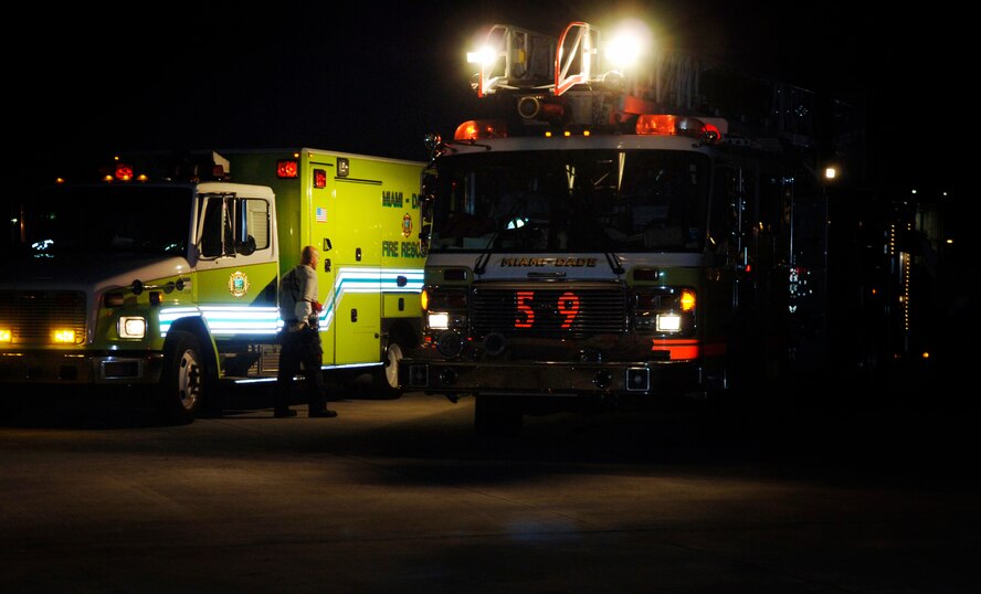 A fire truck and ambulance from Miami-Dade Fire Rescue sit on the tarmac of Miami International Airport in the pre-dawn darkness waiting to accept critical-care patients from an Air Force aermoedical evacuation flight Jan. 23. (U.S. Air Force photo by 2nd Lt. Nicholas Mercurio/Released)