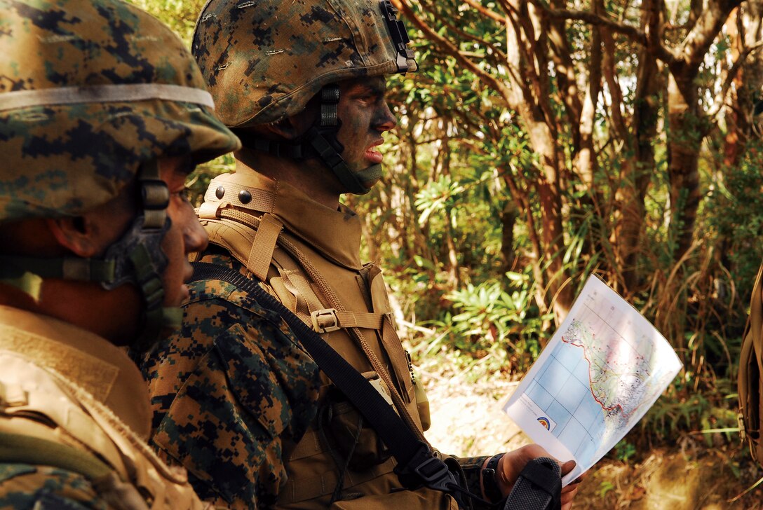 Lance Cpl. Robert Mendez, an intelligence specialist with 12th Marine Regiment, 3rd Marine Division, III Marine Expeditionary Force, observes as Pfc. Brandon Freeman, a training clerk with Headquarters Battery, 12th Marines, consults his map before entering the woods during the land navigation portion of a field skills training exercise at Landing Zone Crow in the Central Training Area Jan. 26.