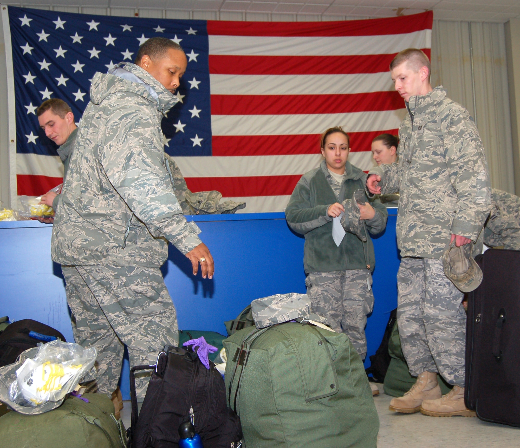 Staff Sgt. Willie Lennon, a services journeyman with the 103rd Force Support Squadron, accounts for his personal bags and military bags before weighing them on scales to be put on a C-21 aircraft. Tech. Sgt. Chris Jones, training manager for the 103rd Force Support Squadron and assistant team leader for the deployers (far right) ensures all equipment and bags are accounted for. (U.S. Air Force photo by Tech. Sgt. Joshua Mead)