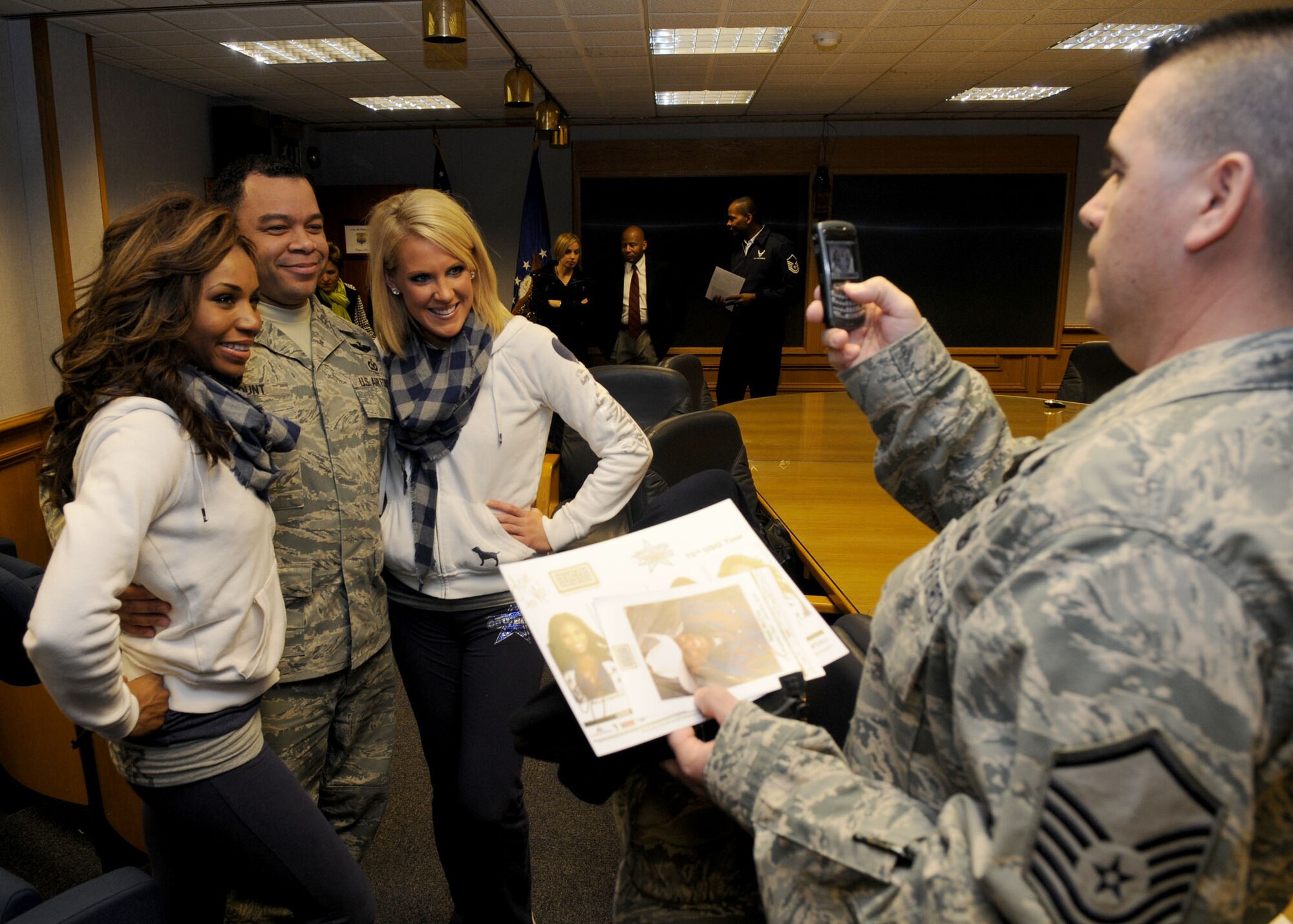 RAF MILDENHALL, England – Tech. Sgt. Benjamin Blount, 100th Air Refueling Wing noncommissioned officer in charge of ground safety programs, poses with Nicole Hamilton and Sarah Gourley, members of the Dallas Cowboys Cheerleading Squad, while Master Sgt. William Rathbun, 100th Air Refueling Wing ground safety manager, takes their photo inside the wing headquarters conference room Jan. 25. Country singer Neal McCoy, along with four cheerleaders with the Dallas Cowboys met with Mildenhall servicemembers during the United Services Organization European Tour January 2010. (U.S. Air Force photo/ Staff Sgt. Jerry Fleshman)