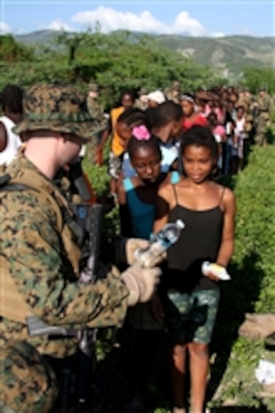 A U.S. Marine from Weapons Company, Battalion Landing Team, 3rd Battalion, 2nd Marine Regiment, 22nd Marine Expeditionary Unit hands a bottle of water to a Haitian girl in Cotes De Fer, Haiti, on Jan. 21, 2010.  Marines and sailors from the 22nd Marine Expeditionary Unit set up a temporary relief-supply distribution point near Cotes de Fer bringing in bottled water and food.  The 22nd Marine Expeditionary Unit, embarked aboard the ships of the Bataan Amphibious Ready Group, is deployed in support of relief operations in Haiti following the 7.0 magnitude earthquake that struck Haiti on Jan. 12, 2010.  