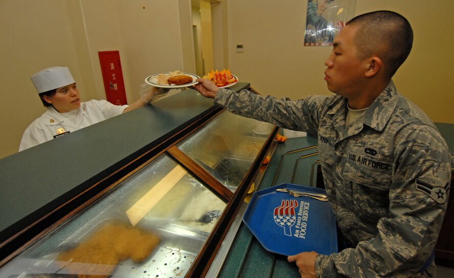 Army Spc. Tracy Bennett, 1-1 Air Defense Artillery, serves dinner to Airman 1st Class Joshua Ahn, 18th Equipment Maintenance Squadron, at the Marshall Dining Facility Jan. 27. The 18th Force Support Squadron, which serves more than 500,000 customers at the dining facilities each year, will be graded by experts in the food and services industry as part of the Air Force Hennessy food service excellence award. (Air Force/Staff Sgt. Jason Lake)