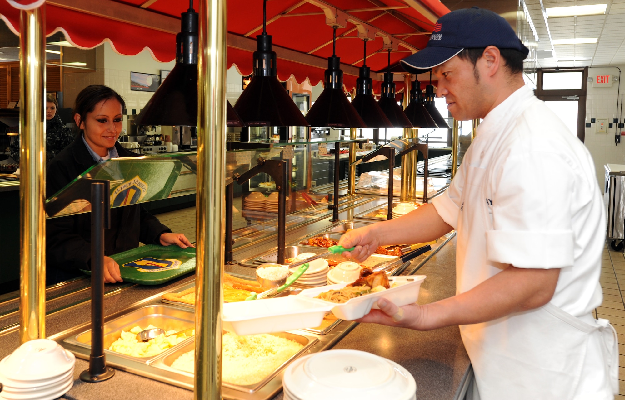 MISAWA AIR BASE, Japan – Sator Numayana, Grissom Dining Facility prep cook, fills the to-go box of Petty Officer 2nd Class Amarylis Lunavaldez, Naval Communications Telecom Systems Far East Detachment store keeper Jan. 26 at the Grissom Dining Facility. The DFAC is open to all ranks and services. (U.S. Air Force photo/Staff Sgt. Phillip Butterfield)