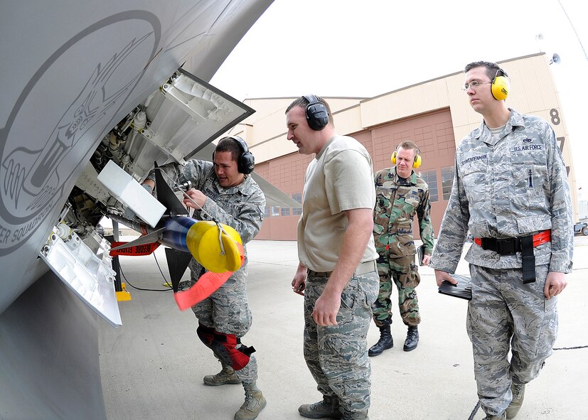 HOLLOMAN AIR FORCE BASE, N.M. -- Staff Sgt.  Christopher Osterholm and Airman 1st Class Patrick Roberts, 49th Aircraft Maintenance Squadron, load a weapon on the F-22 Raptor as the Load Crew of the Year competition inspection team looks on, Jan. 19. Sergeant Osterholm and his crew advanced in the tournament by defeating another load crew the previous week. (U.S. Air Force photo by Senior Airman John Strong)