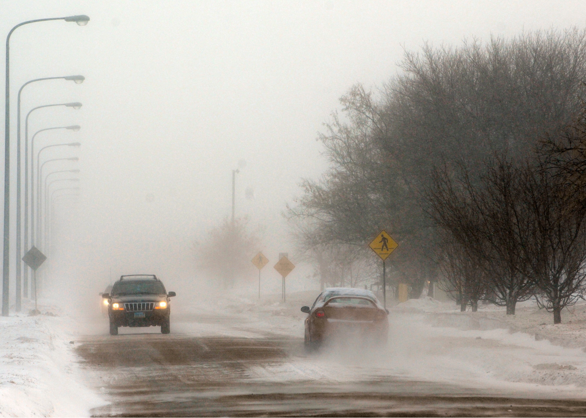 MINOT AIR FORCE BASE, N.D. -- Vehicles drive through heavy winds and snow drifts here Jan. 25. The winds reached speeds as quick as 36 mph and sustained at 35 mph. Heavy winds and snow fall created prime conditions for whiteouts. (U.S. Air Force photo by Airman 1st Class Ashley N. Avecilla)