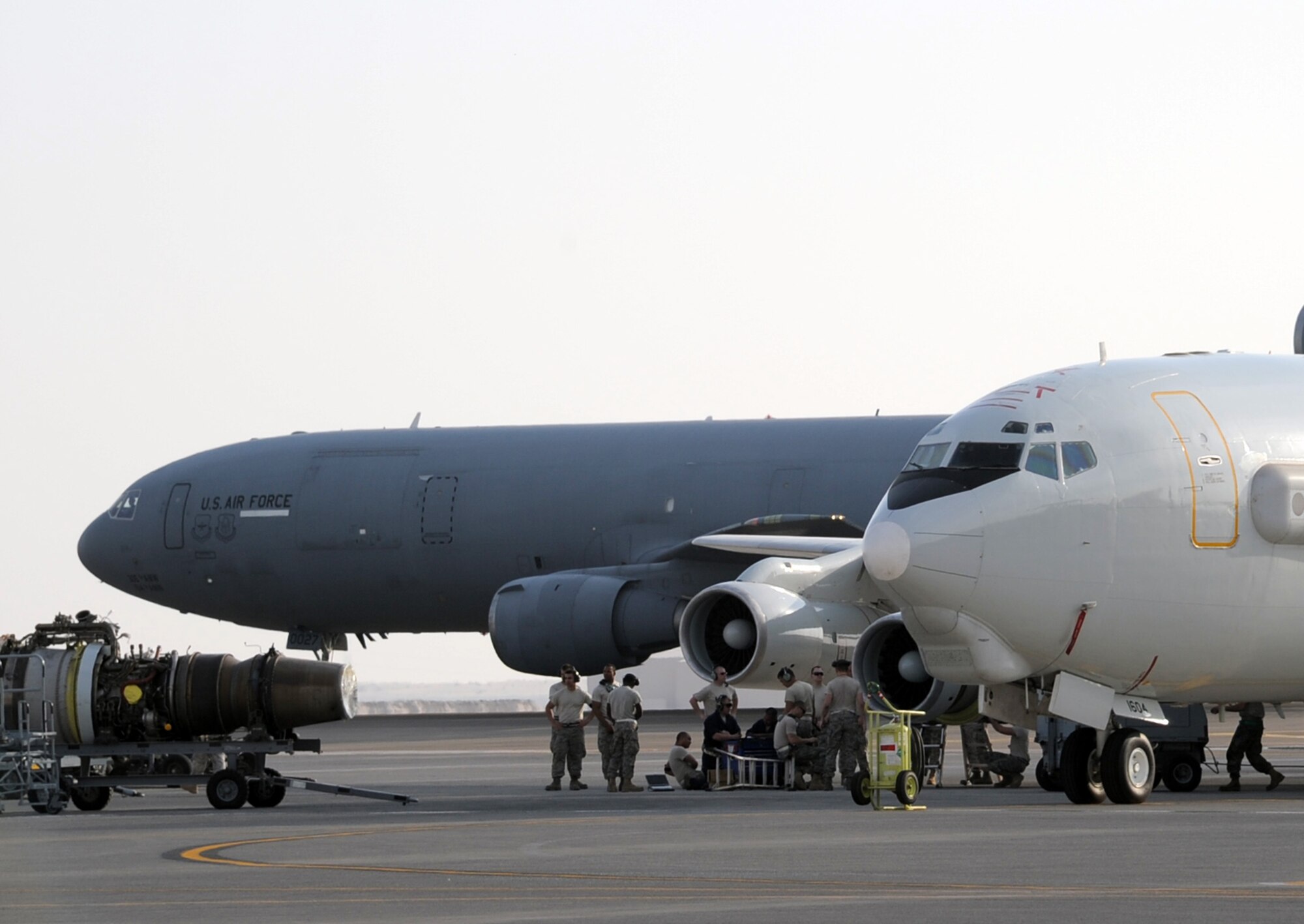 Maintenance Airmen work on an E-3 Sentry Airborne Warning and Control System aircraft while a KC-10 moves past behind them during operations on the flightline at a non-disclosed base in Southwest Asia on Jan. 23, 2010.  The E-3, assigned with the 965th Airborne Air Control Squadron of the 380th Air Expeditionary Wing, is a modified Boeing 707/320 commercial airframe with a rotating radar dome that provides situational awareness of friendly, neutral and hostile activity, command and control of an area of responsibility, battle management of theater forces, all-altitude and all-weather surveillance of the battle space, and early warning of enemy actions during joint, allied, and coalition operations. (U.S. Air Force Photo/Tech. Sgt. Scott T. Sturkol/Released)