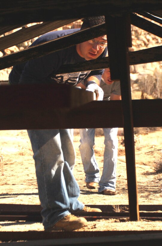 Lance Cpl. Nick Trevino, a motor transport operator with Support Company, 3rd Combat Engineer Battalion, slides a piece of wood under the roof of a cabin to help support the fragile structure at Keys Ranch in Joshua Tree National Park Jan. 28. Trevino and 13 other Marines and sailors volunteered to help restore the cabin which had succumbed to the harsh climate of the Mojave Desert and remove unwanted vegetation from the ranch.