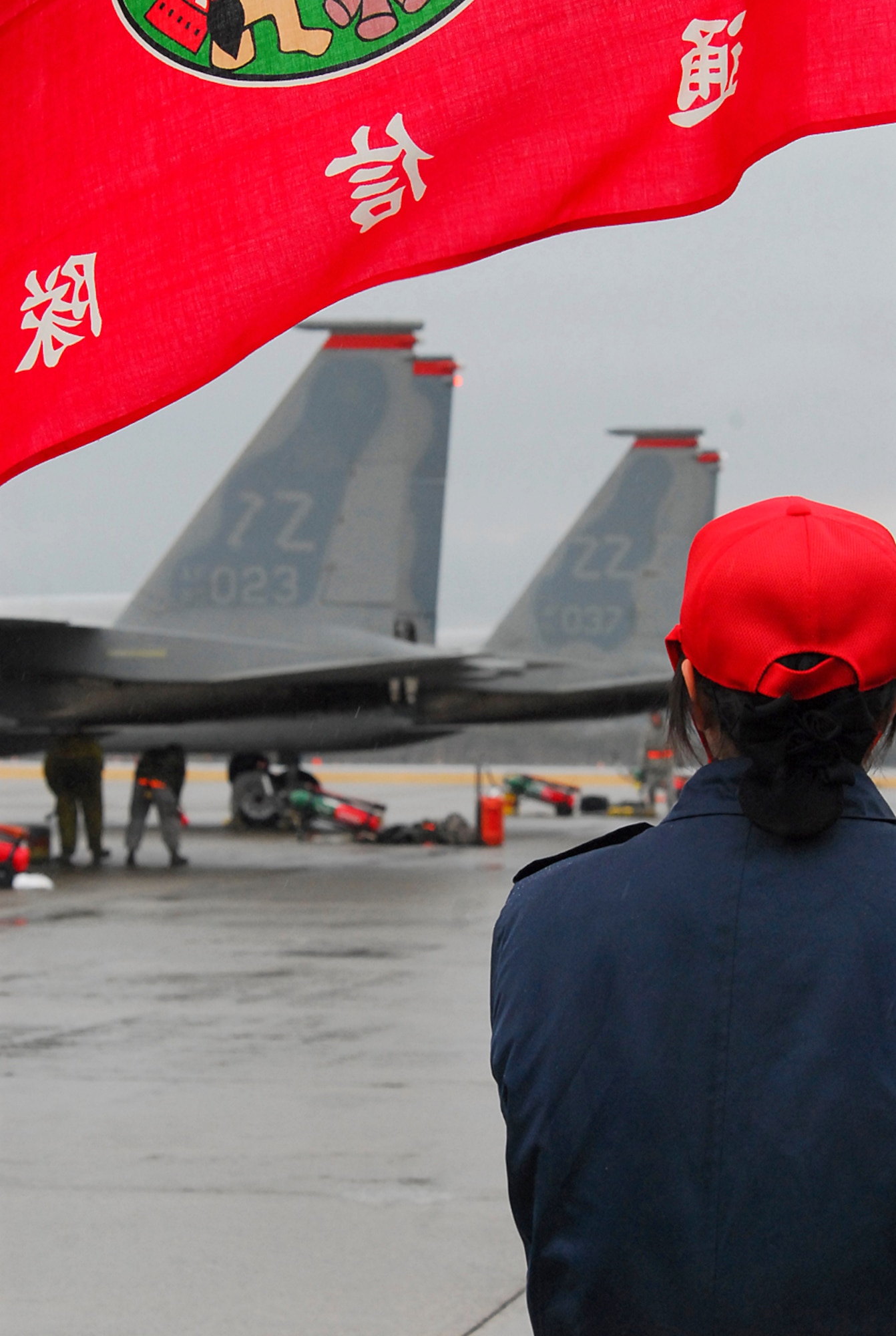 An airman from the Japan Air Self Defense Force communications squadron at Hyakuri Air Base holds her unit's flag as part of a formation to greet Airmen from the 67th Fighter Squadron. Airmen and F-15Cs from Kadena are operating from the base, which sits about 70 miles north of Tokyo, as part of an aviation training relocation. The Airmen will spend the next eight days flying alongside and with their Japanese counterparts. (U.S. Air Force photo / 1st Lt. Bryan Bouchard)