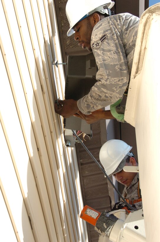 Airman 1st Class Odey Igbaji, 316th Civil Engineer Squadron electrical systems apprentice, top, and Airman 1st Class Victor Gonzalez Dias, 316 CES electrical systems apprentice, bottom, upgrade a light fixture on the library Bldg. 1642, from inside an aerial lift truck Jan. 14, 2010. (U.S. Air Force photo by Bobby Jones)