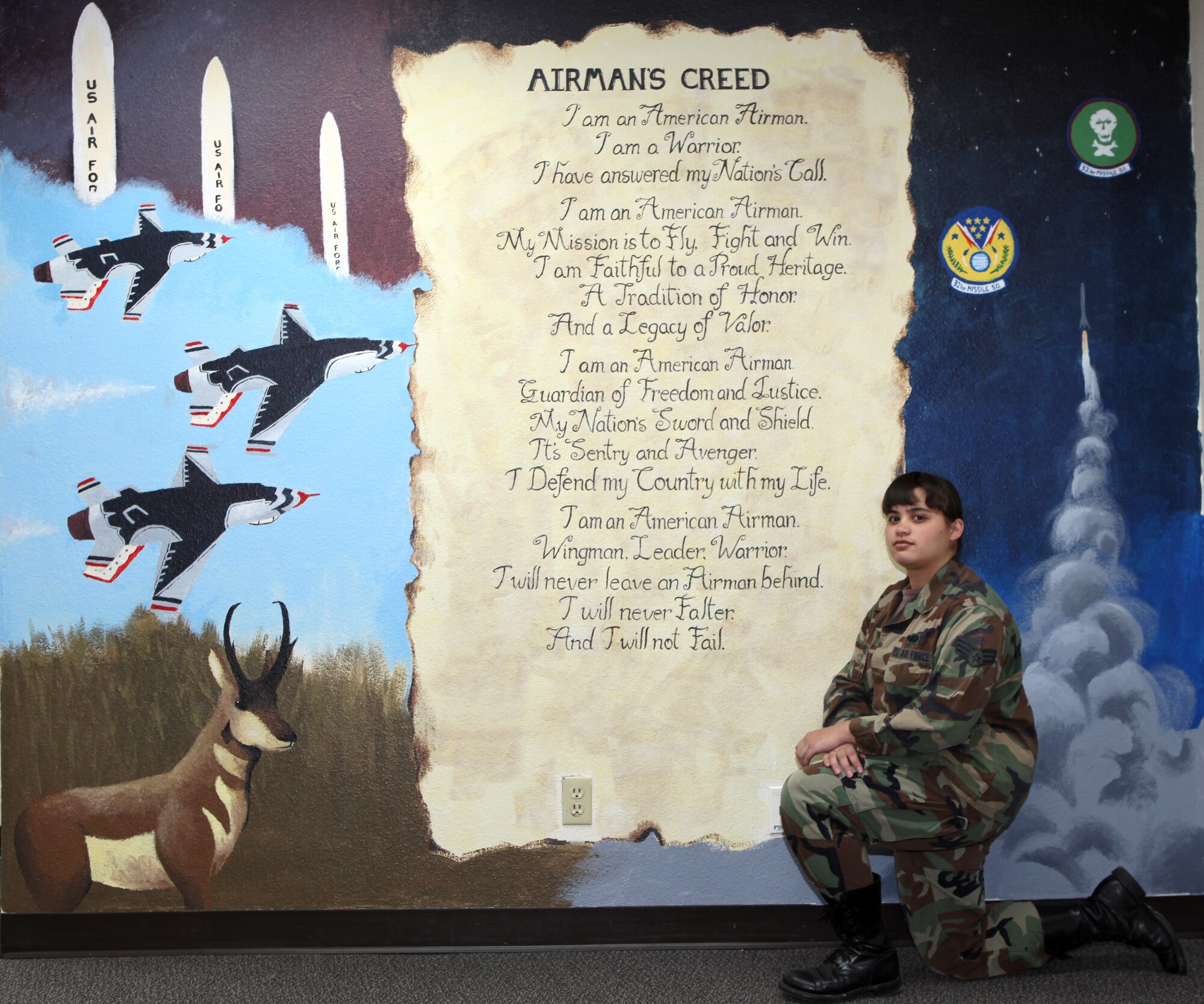 Senior Airman Stephanie Scarset, 321st Missile Squadron, poses with the mural she painted. Her mural encompasses the Air Force Creed, images of Warren and the Air Force demonstration team, the Thunderbirds. (U.S. Air Force photo/Berni Ernst) 