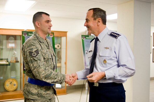 Gen. Raymond E. Johns, Jr., commander of Air Mobility Command, "coins" Staff Sgt. Delmer Hively, 62nd Maintenance Operations Squadron, while visiting the 62nd Airlift Wing headquarters building Monday. General Johns attended a joint basing briefing, met with McChord Airmen and civilian employees, and walked through the customer service mall during his tour of Bldg. 100. (U.S. Air Force Photo/Abner Guzman)