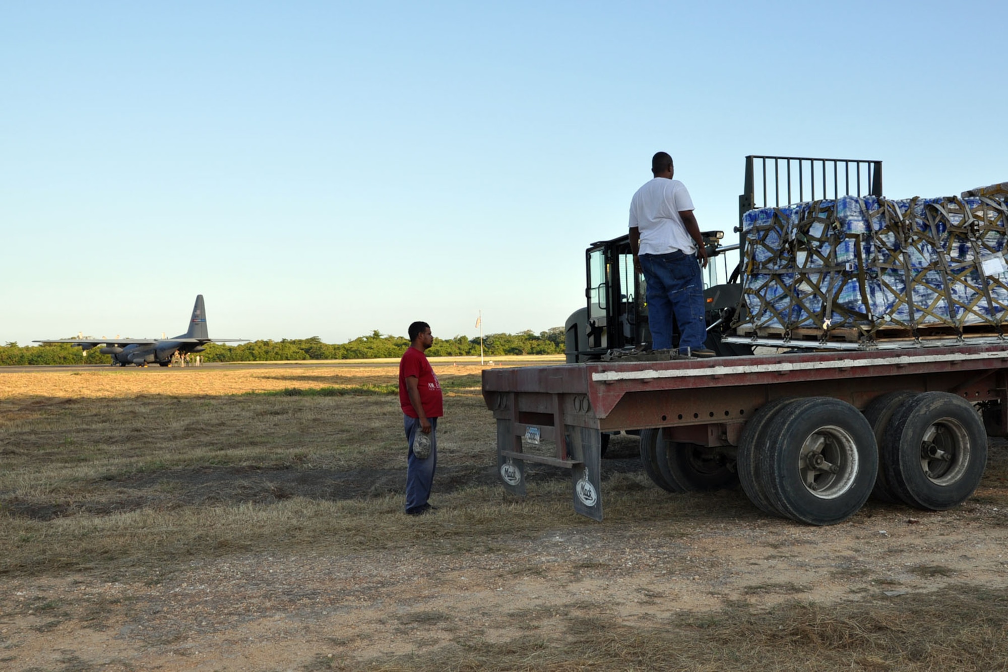SAN ISIDIRO AIR BASE, Dominican Republic -- Workers observe as a forklift lowers a pallet of cargo on to the bed of a truck sitting just off the tarmac here, January 21. A C-130H Hercules cargo aircraft, assigned to the U.S. Air Force Reserve's 910th Airlift Wing can be seen in the background. The aircraft, based at Youngstown Air Reserve Station, Ohio, just delivered a cargo of 18,400 pounds of food and water to the air base, located just outside of the Dominican capital of Santo Domingo. From here, it will be trucked across the island to Port-au Prince, Haiti as part of the massive international effort to provide relief to the people of the Caribbean island nation in the aftermath of a devastating January 12 earthquake. U.S. Air Force photo by Master Sgt. Bob Barko Jr.
