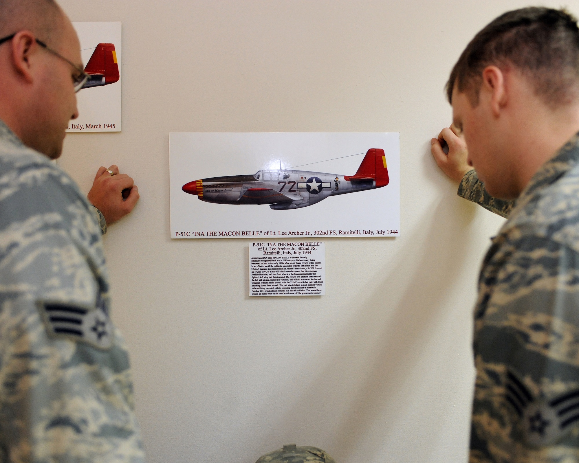 Two current members of the 332nd Air Expeditionary Wing reflect on the achievements of retired Lt. Col. Lee A. Archer at a display honoring his legacy in the wing headquarters building at Joint Base Balad, Iraq, Jan. 30. Colonel Archer, one of the unit’s original Tuskegee Airmen, passed away Jan. 27 in New York at the age of 90. (U.S. Air Force photo by Tech. Sgt. Linda C. Miller/Released)