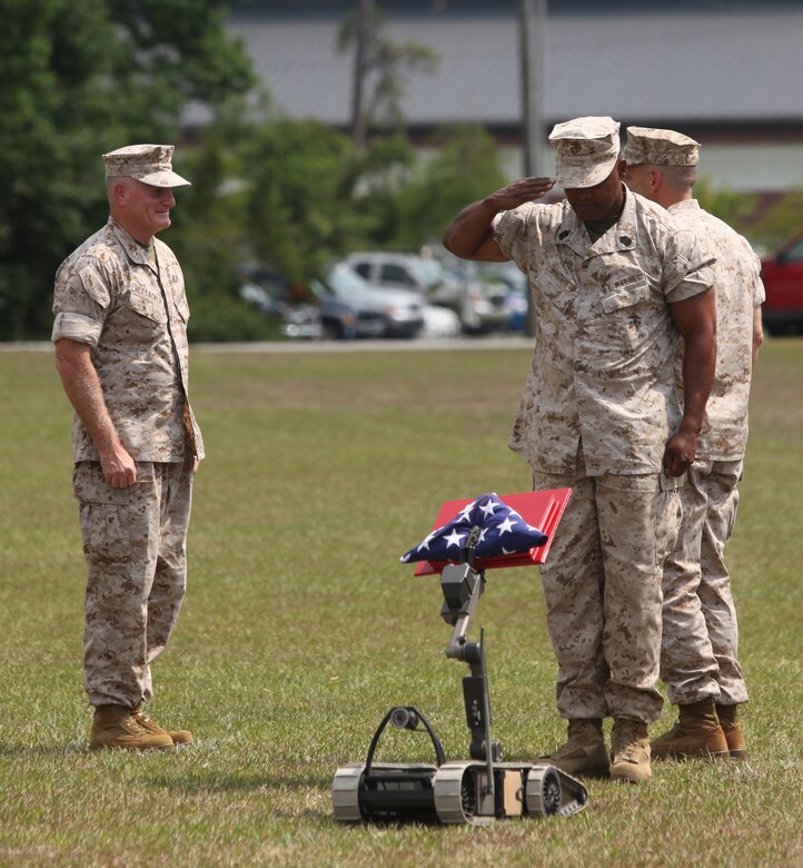 Sgt. Maj. Efren Z. Whitehead (right), sergeant major of the Marine Corps Engineer School, Marine Corps Base Camp Lejeune, salutes the American flag delivered by the 310SUG-V counter-improvised explosive device robot during a retirement ceremony for Col. David S. Heesacker, commanding officer of MCES, at Courthouse Bay aboard the base, July 1.  Heesacker is retiring from the Marine Corps after 32 years of active-duty service.