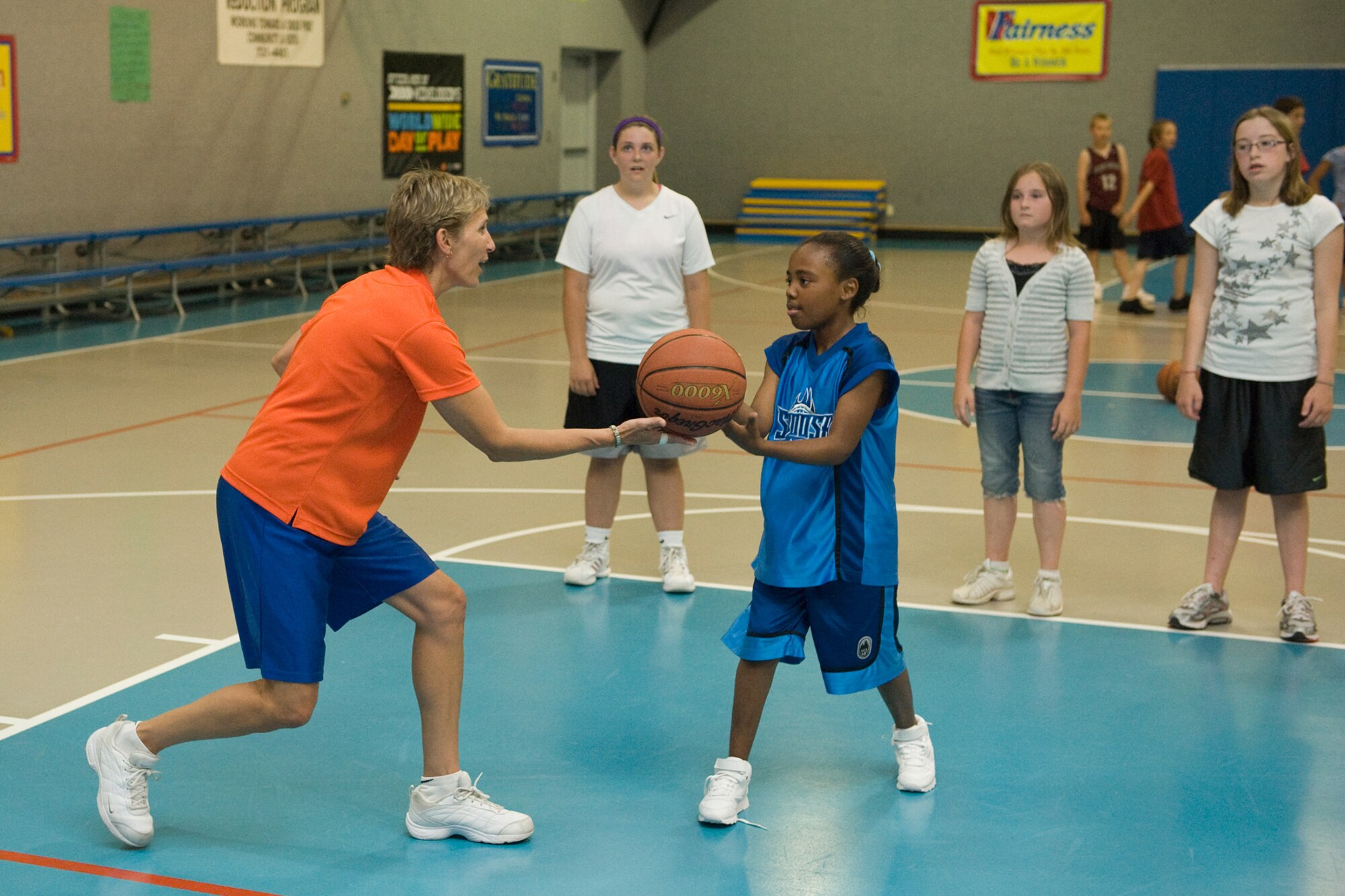 Sandy Slade assists Chloe Hawkins after an attemped shot during the Skillastics basektball clinic June 29 at the Youth Activities Center gym. Other summer camp participants listen in. (U.S. Air Force Photo/Beau Wade)