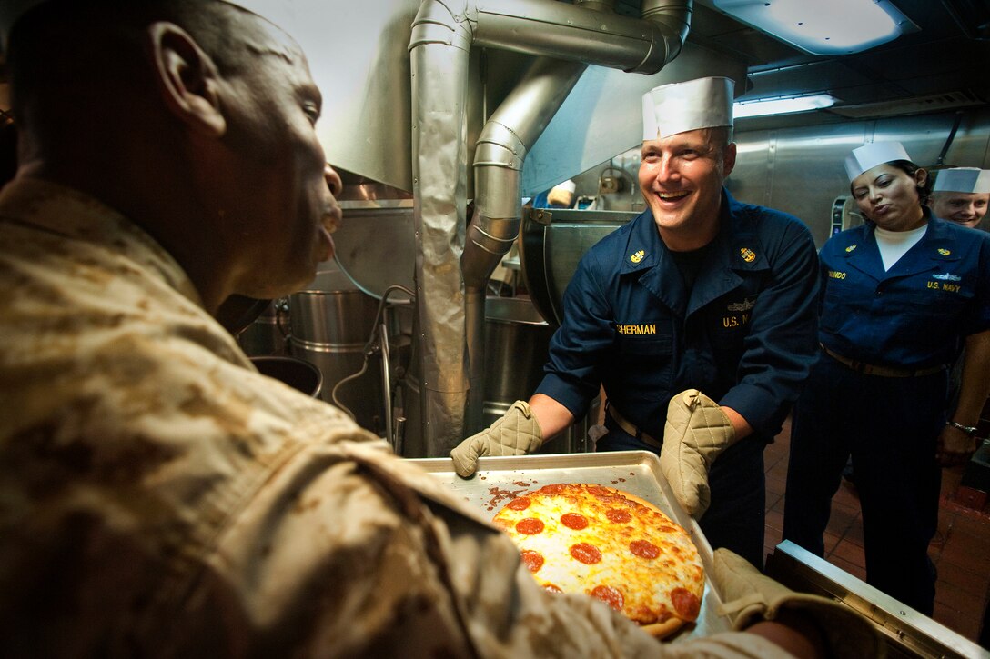 U.S. Navy Chief Chris Sherman, a yeoman assigned to Amphibious Squadron 5, hands a tray of pizzas to U.S. Marine Corps Master Gunnery Sgt. Erik Jackson while they and other senior enlisted sailors and Marines make dinner aboard the USS New Orleans underway in the Pacific Ocean, June 27, 2010. 