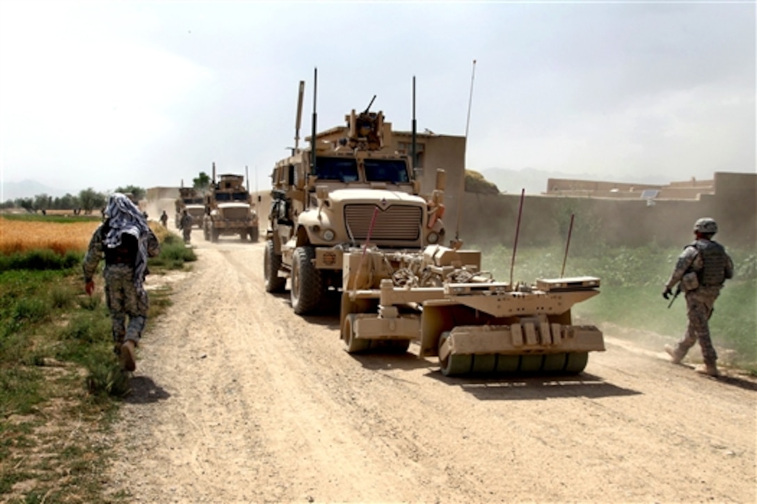 U.S. Army soldiers walk through the village of Kotub Kheyl in Logar province, Afghanistan, as a convoy of Mine Resistant Ambush Protected vehicles passes by, June 24, 2010. The soldiers are assigned to the 401st Military Police Company, 720th MP Battalion, 89th MP Brigade.