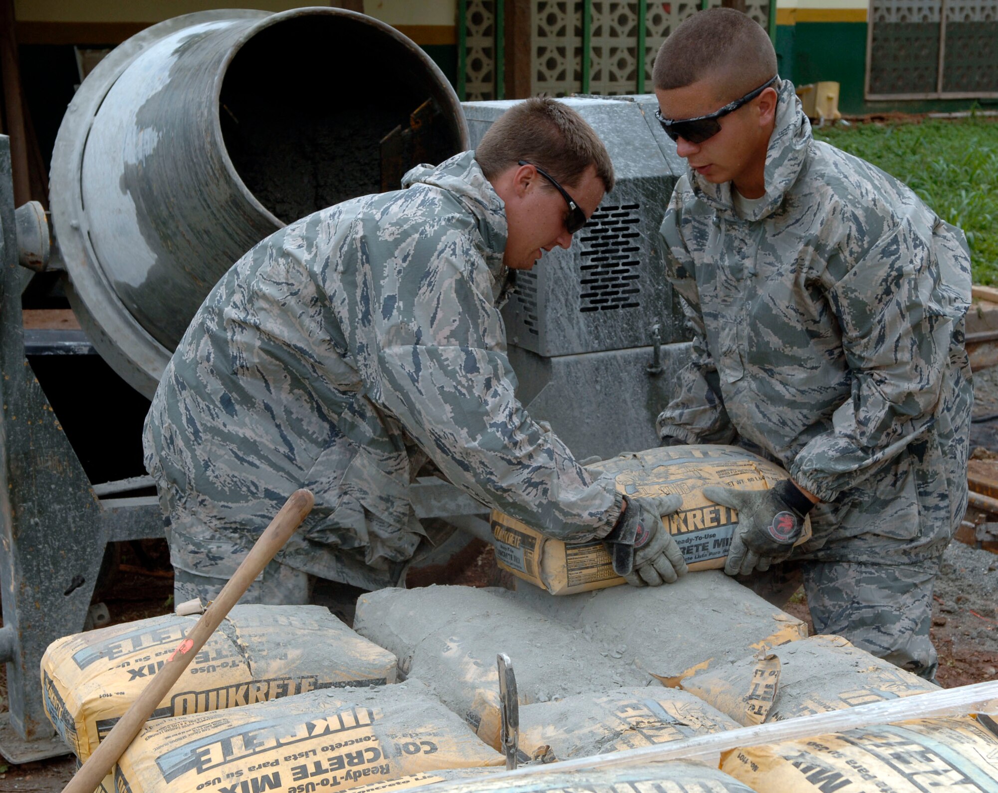 Airman 1st Class Sean Melville (left) and Airman 1st Class Joseph Evanhoff, 820th Expeditionary RED HORSE Squadron, pour bags of concrete into a mixer at Rio Iglesia Medical Clinic July 2. (U.S. Air Force photo/Tech. Sgt. Eric Petosky)