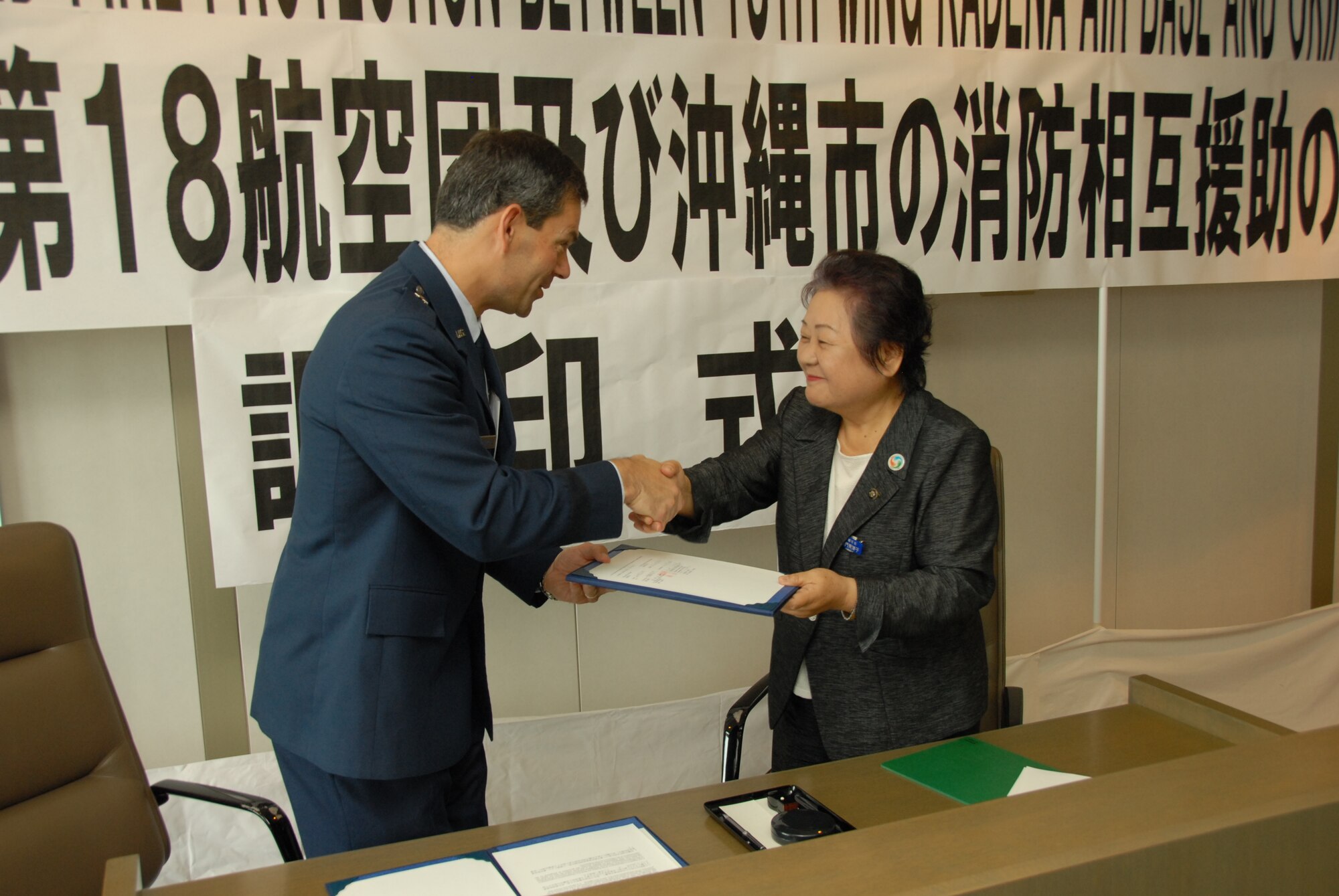 Brig. Gen. Ken Wilsbach, 18th Wing commander, and Ms Mitsuko Tomon, Okinawa City mayor, shake hands after signing a memorandum of understanding to formalize cooperation between their respective fire departments July 2, 2010 at the Okinawa City mayor's office. The MOU establishes a framework for mutual aid in the case of fire emergencies. (U.S. Air Force photo/Junko Kinjo)