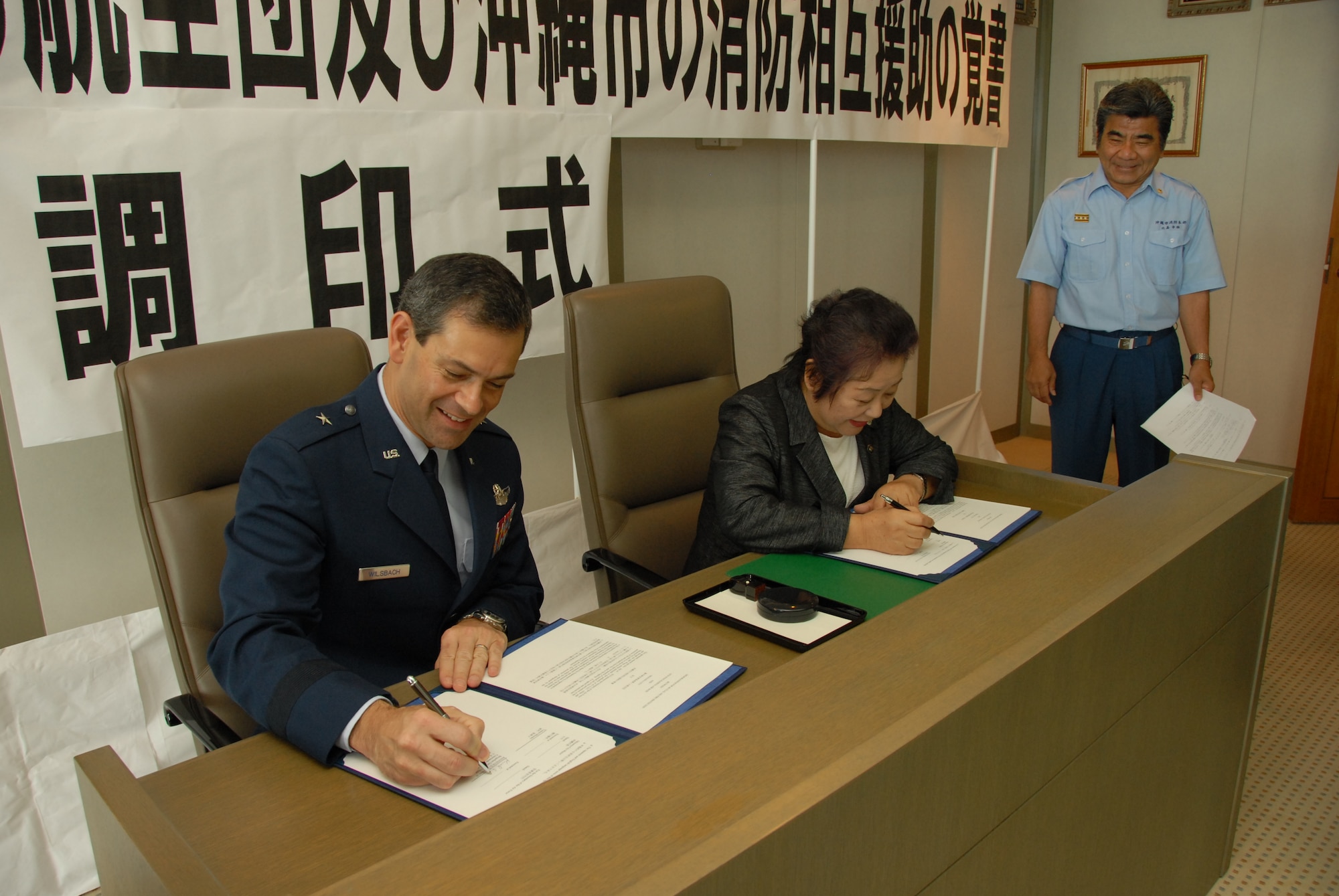 Brig. Gen. Ken Wilsbach, 18th Wing commander, and Ms Mitsuko Tomon, Okinawa City mayor, sign a memorandum of understanding to formalize cooperation between their respective fire departments July 2, 2010 at the Okinawa City mayor's office. The MOU establishes a framework for mutual aid in the case of fire emergencies. (U.S. Air Force photo/Junko Kinjo)