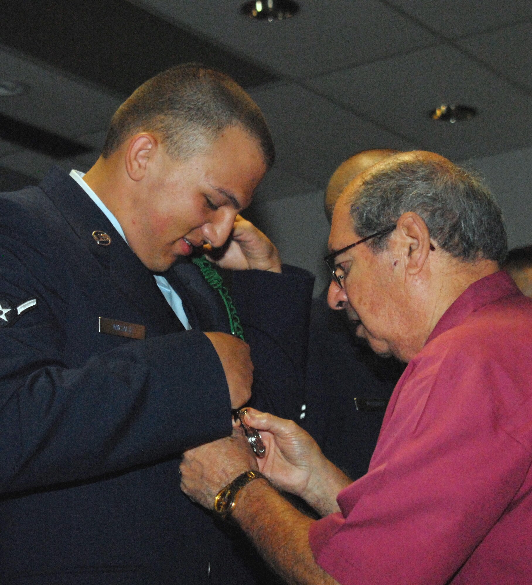 Airman 1st Class Laurence Micale watches as his grandfather, retired Col. Peter Micale III, pins on his new fire protection badge during the graduation ceremony July 1. Airman Micale is a third generation Air Force member with family ties going back to the start of the Air Force. (U.S. Air Force photo/Connie Hempel)