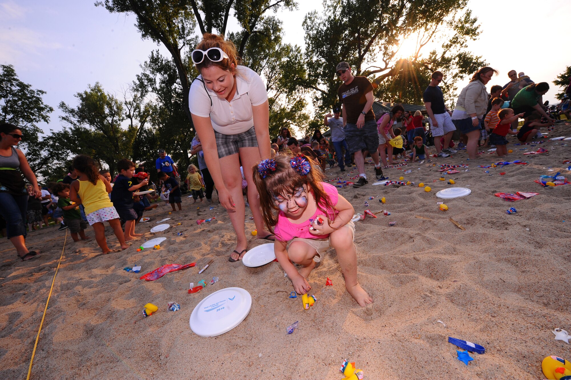 OFFUTT AIR FORCE BASE, Neb. - Three year old Madison Melloy, daughter of Senior Airman Andrew Melloy, assigned to the 20th Intelligence Squadron, grabs a fist full of prizes from the base lake's sand volleyball  pit while attending the Red, White and Blue annual fireworks display July 2.  Several family activities took place at the celebration including appearances by a professional magician and a small play given by Prairied Treasure Melodrama. U.S. Air Force photo by Josh Plueger
