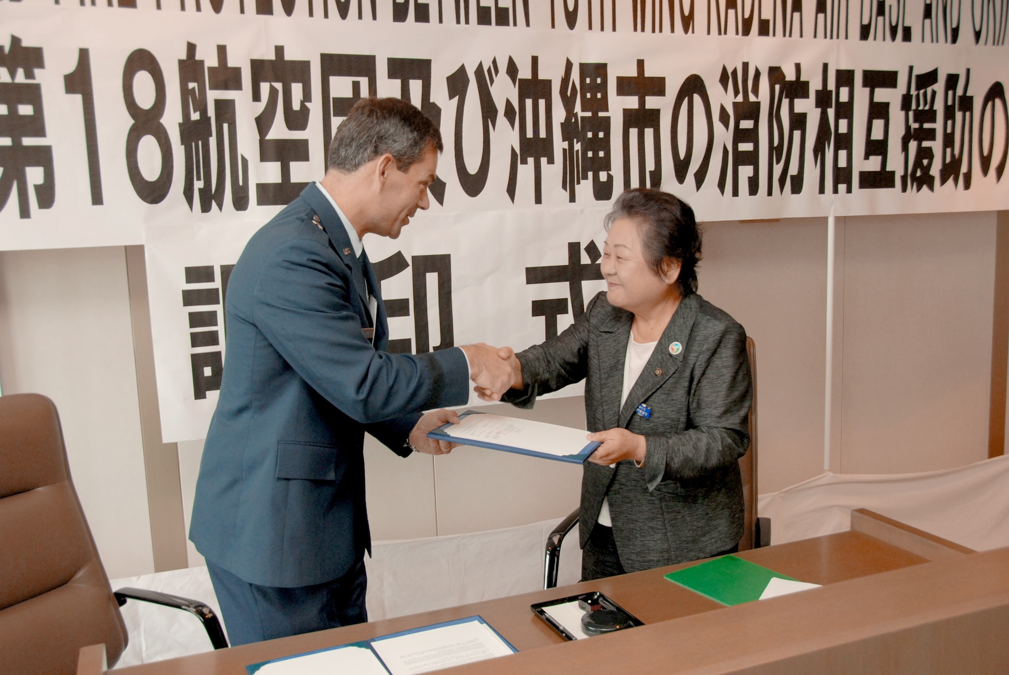 Brig. Gen. Ken Wilsbach and Mitsuko Tomon shake hands after signing a memorandum of understanding to formalize cooperation between their respective fire departments July 2, 2010, in Okinawa, Japan. The MOU establishes a framework for mutual aid in the case of fire emergencies. General Wilsbach is the 18th Wing commander. Ms. Tomon is the mayor of Okinawa City. (U.S. Air Force photo/Junko Kinjo)