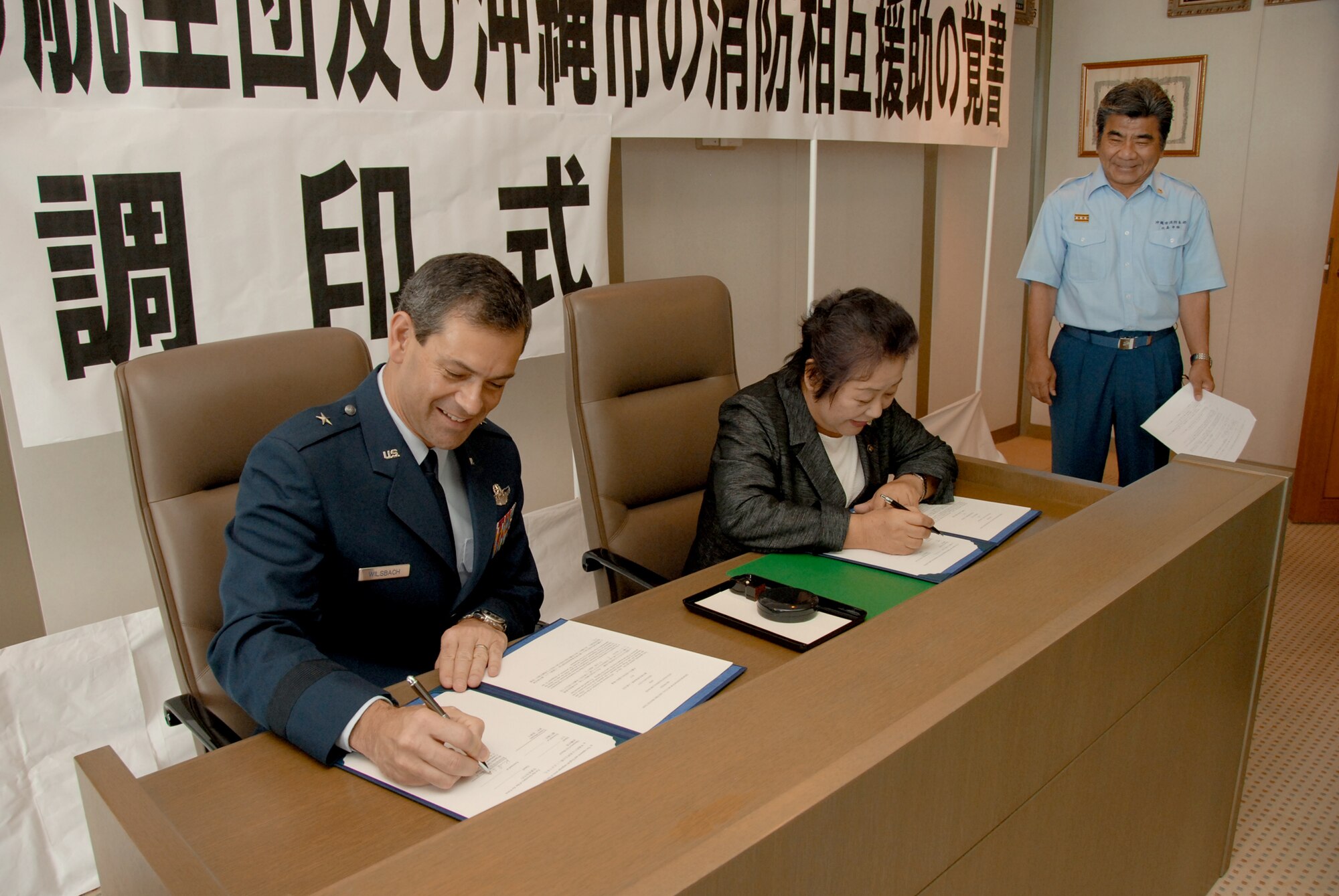 Brig. Gen. Kenneth S. Wilsbach and Mitsuko Tomon sign a memorandum of understanding to formalize cooperation between their respective fire departments July 2, 2010, in Okinawa, Japan. The MOU establishes a framework for mutual aid in the case of fire emergencies. General Wilsbach is the 18th Wing commander. Ms. Tomon is the mayor of Okinawa City. (U.S. Air Force photo/Junko Kinjo)