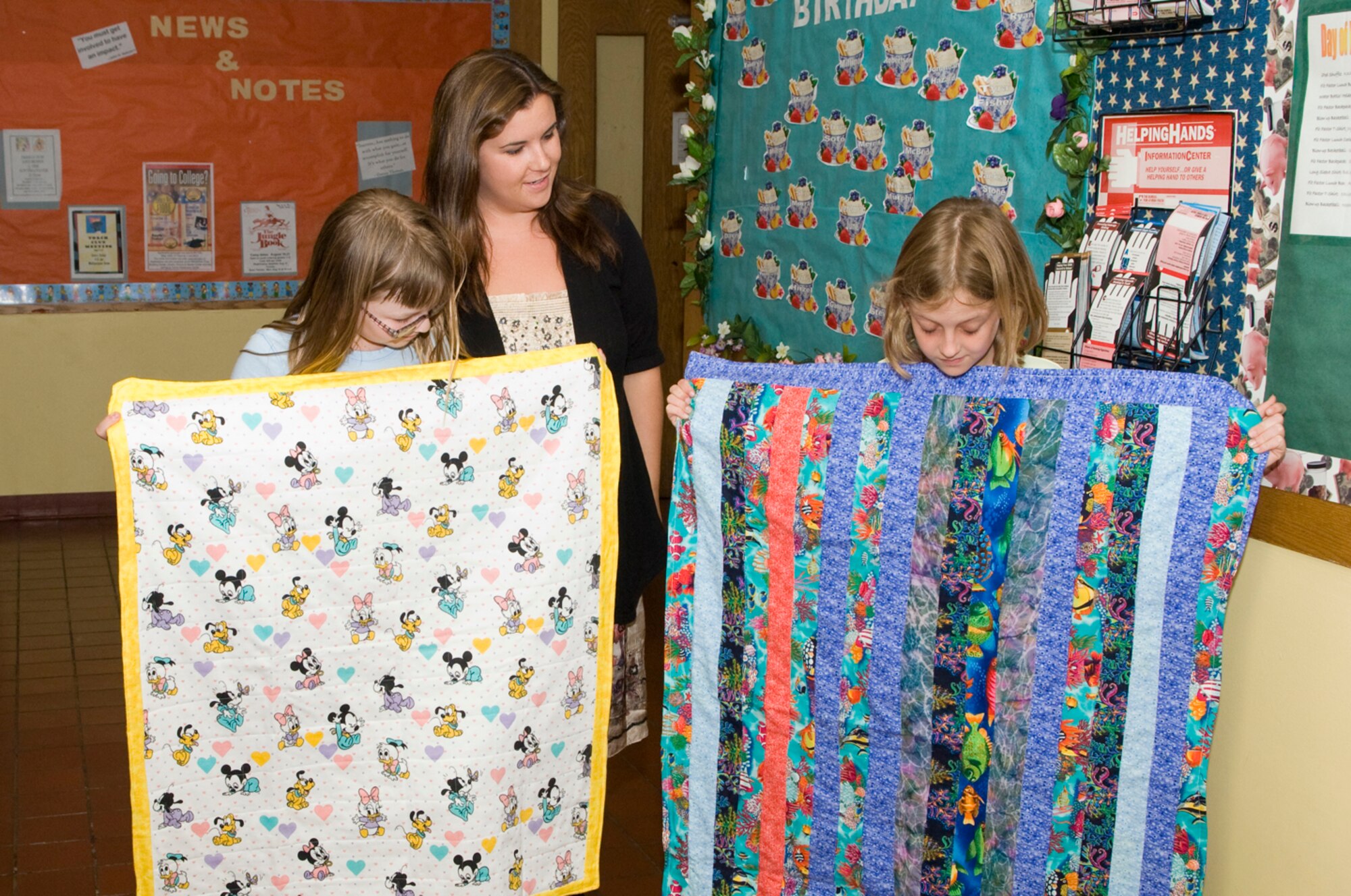 HANSCOM AIR FORCE BASE, Mass. – Jade Milliman (left) and Bailee Cox display quilts made by the 4-H Sewing Club while Christina Conzo of the Airmen and Family Readiness Center looks on. The Sewing Club donated four quilts to the A&FRC’s Layette program on June 18 at the Youth Center.  (U.S. Air Force photo by Mark Herlihy)