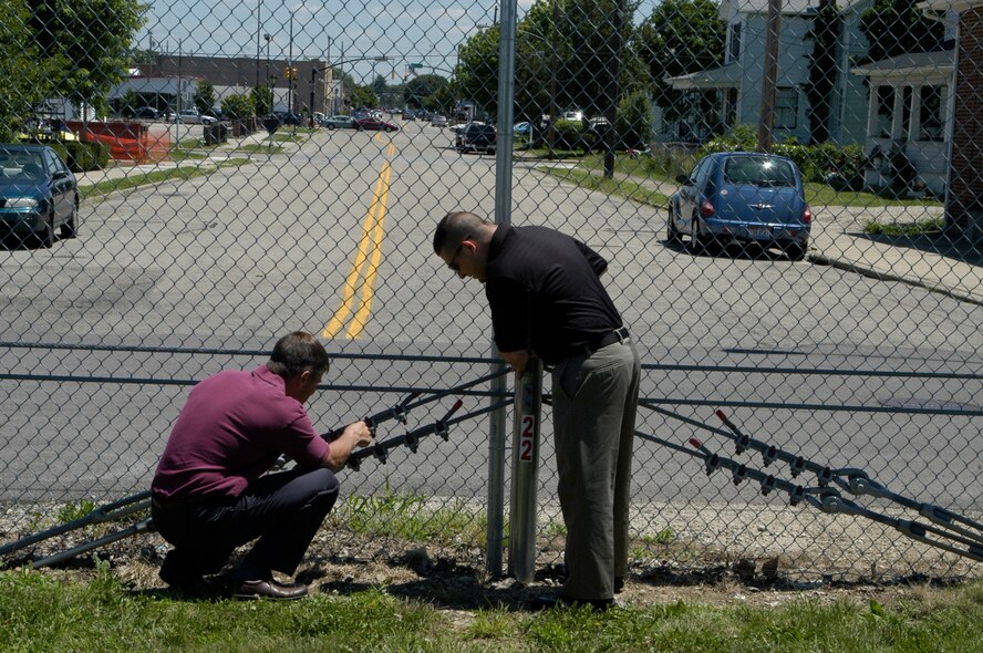 Antiterrorism Installation Officer's Mark Myers and Nick Phillips inspect recently installed fence cabling, which is used to secure safety. 