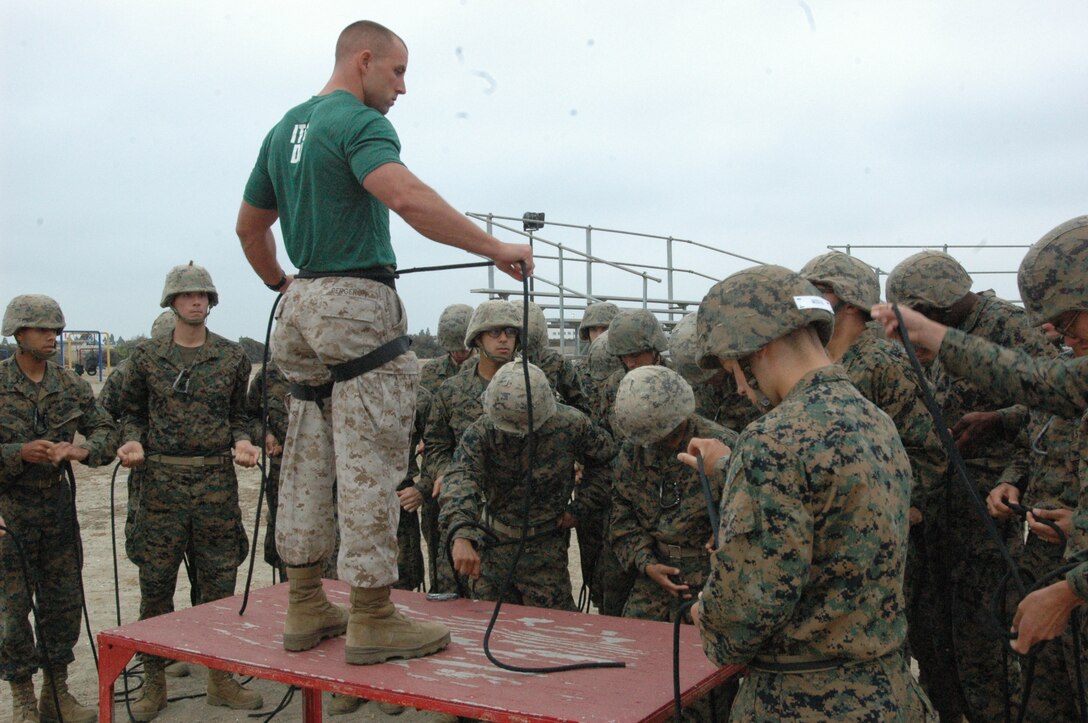 The guides and squad leaders of Company H watch an Instructional Training Company drill instructor demonstrate how to make the safety harness they will be using when wall rappelling here.