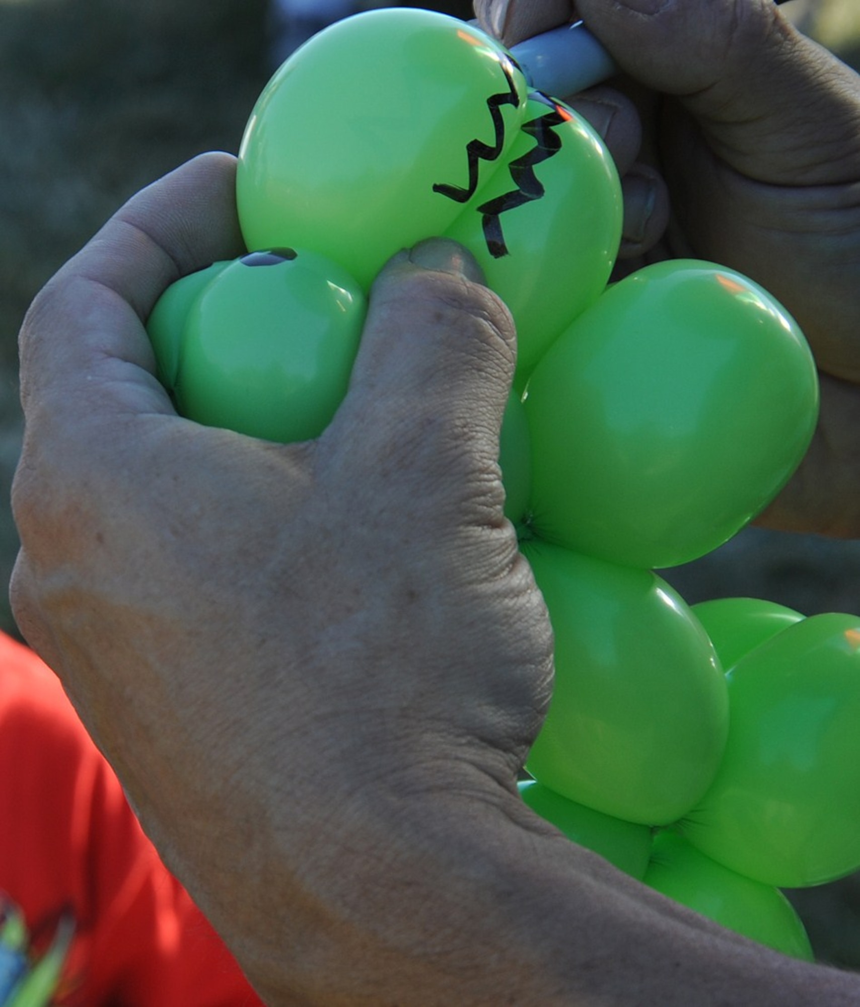 A balloonist puts the finishing touches on a dinosaur balloon animal at Doughboy Field during the Fourth of July celebration. Children were given the opportunity to get their face painted, receive custom balloon animals from balloonist and play in bouncy castles during the celebration. (U.S. Air Force photo/Senior Airman David Carbajal)