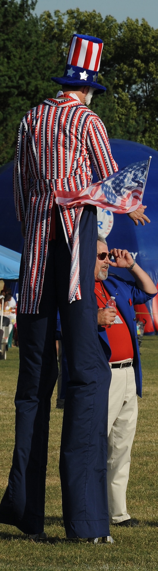 A stilt walker greets one of the event coordinators at Doughboy Field during the Fourth of July celebration. The celebration included bouncy castles, a stilt walker, a magician, a balloonist, face painters, live rock-band performances and a fireworks display. (U.S. Air Force photo/Senior Airman David Carbajal)
