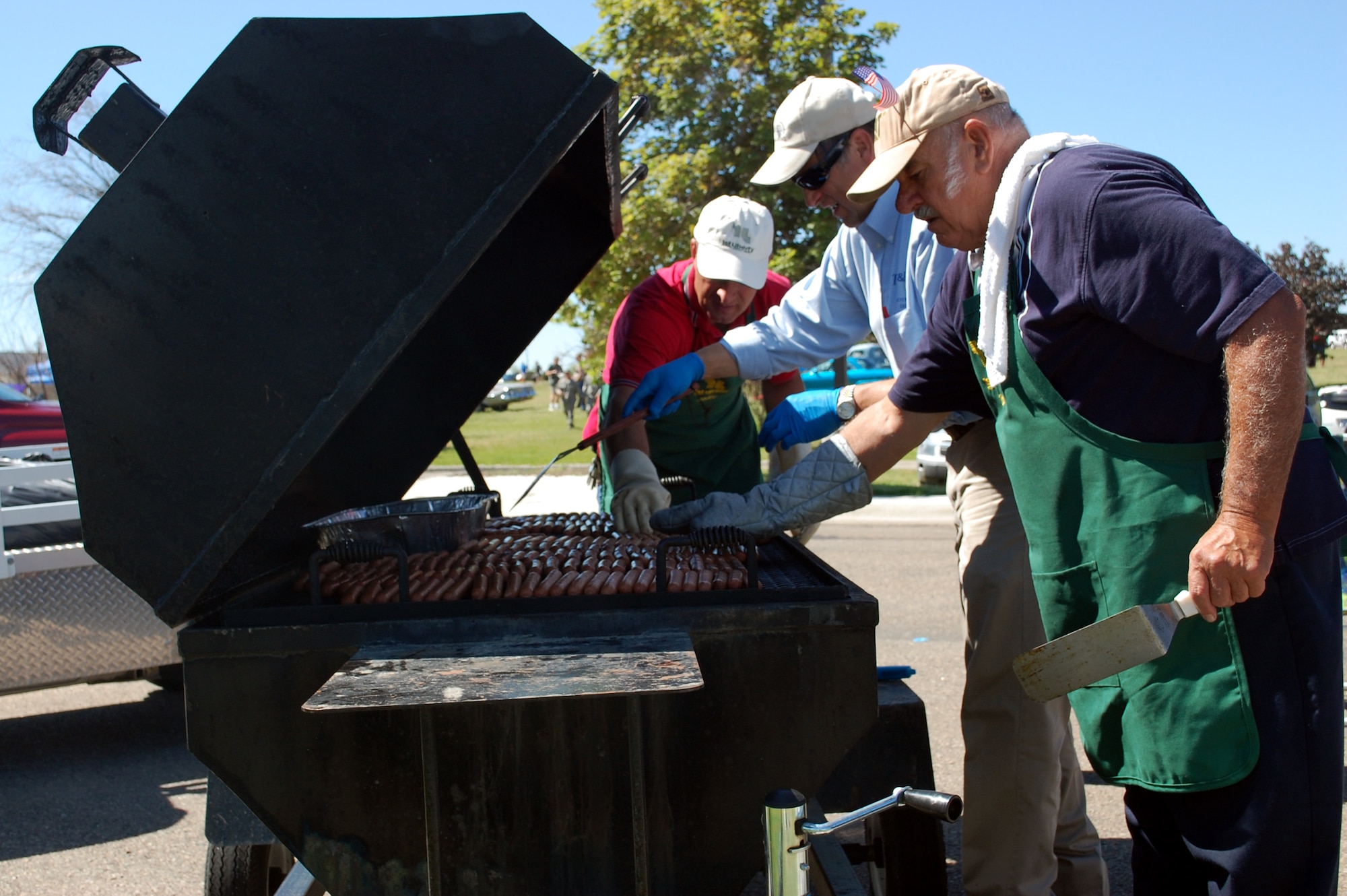 Volunteer cooks, from left to right, Mike Croscutt, Erling Juel and Bob Charpentier, get a jump on cooking hot dogs for the base picnic July 1. Mr. Crosscutt and Mr. Charpentier and both affiliated with 1st Liberty Federal Credit Union and Mr. Juel is a member of the Military Affairs Committee. (U.S. Air Force photo/Valerie Mullett)