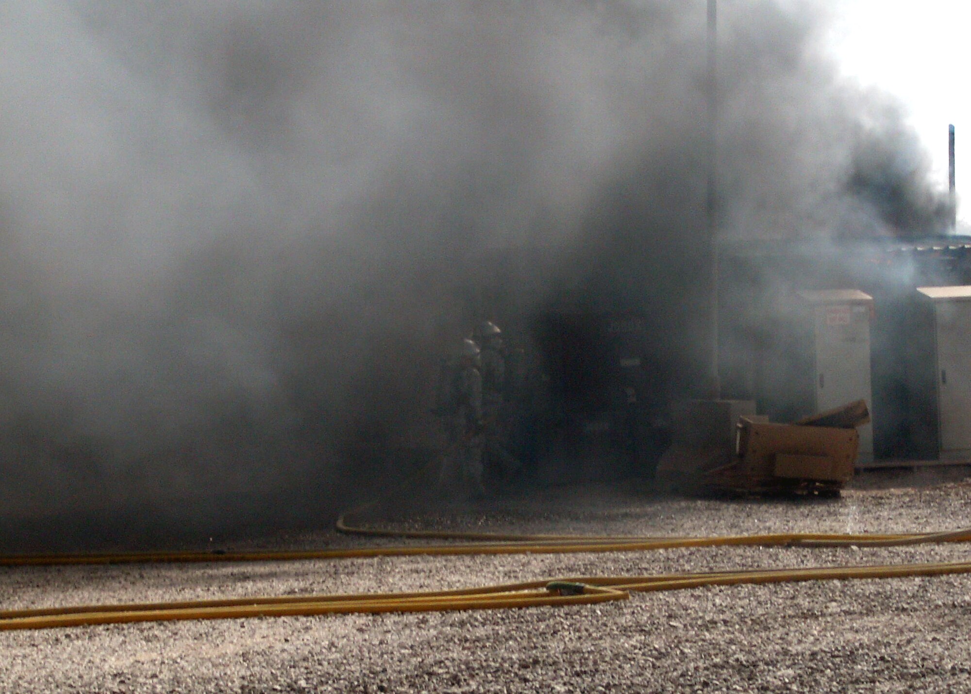 332nd Expeditionary Civil Engineer Squadron Fire Emergency Services Flight firefighters are virtually unseen in the billowing smoke of an air conditioning generator fire July 5, 2010, at Joint Base Balad.  The firefighters had extinguished the visible flames, now they had to go in for a closer look to ensure the fire was completely out.  (U.S. Air Force photo/Courtesy of 332nd Expeditionary Civil Engineer Squadron Fire Emergency Services Flight )