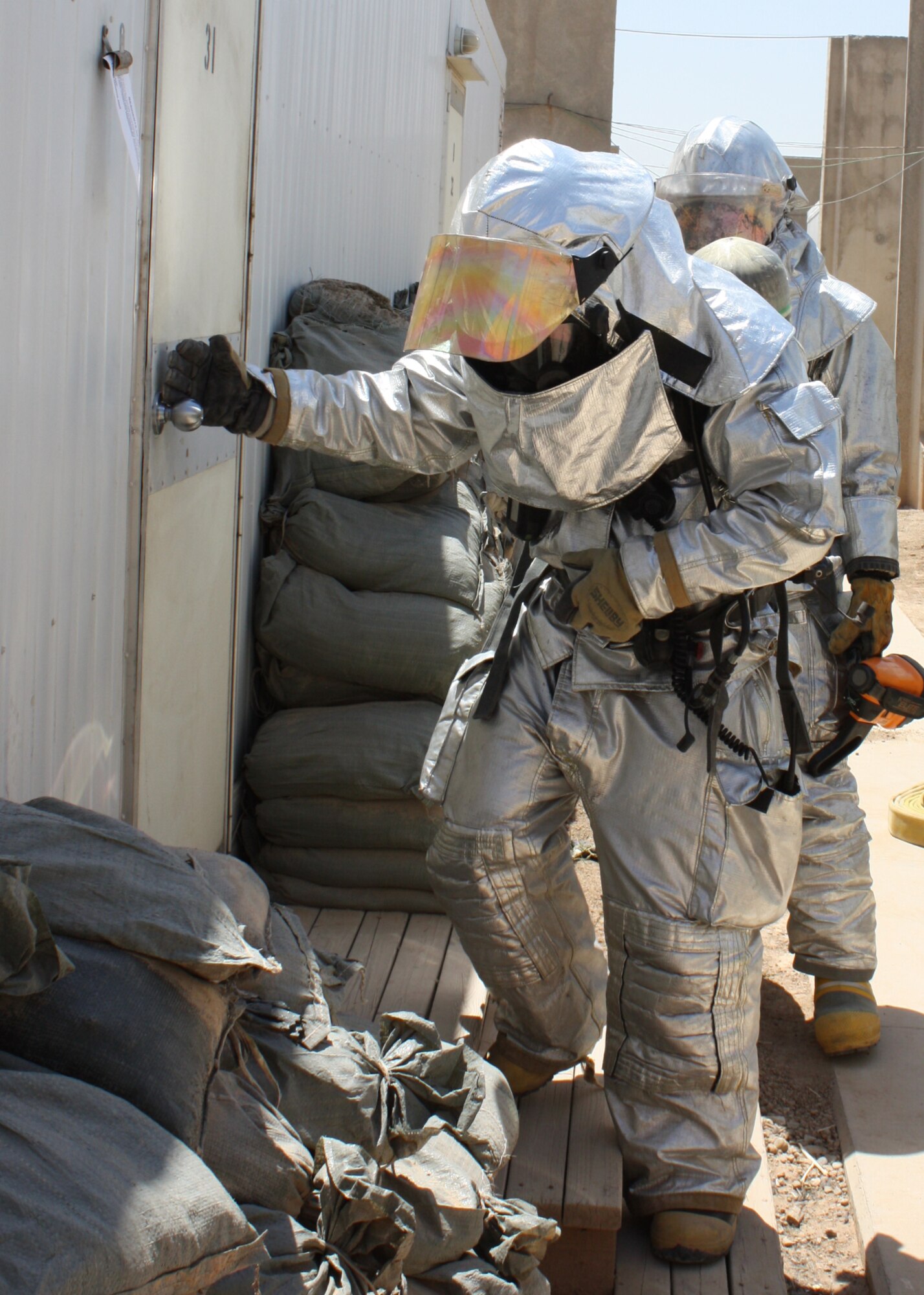Staff Sgt. Gregory Teague and Airman 1st Class Dion Battisti, 332nd Expeditionary Civil Engineer Squadron Fire Emergency Services Flight firefighters, check for heat and smoke before breaking down a door of a containerized housing unit during training at Joint Base Balad, Iraq, July 3, 2010.  The firefighters at Balad are responsible for responding to emergency calls around the entire base. Sergeant Teague is deployed from Dyess Air Force Base, Texas, and Airman Battisti is deployed from Andersen AFB, Guam. (U.S. Air Force photo/Staff Sgt. Stacy Fowler)