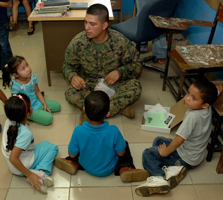 Lance Cpl. Carlos Fuentes, a civil affairs Marine deployed from the 4th Civil Affairs Group, helps children assemble rubber band airplanes at the Sansonsito School July 12. (U.S. Air Force photo/Tech. Sgt. Eric Petosky)