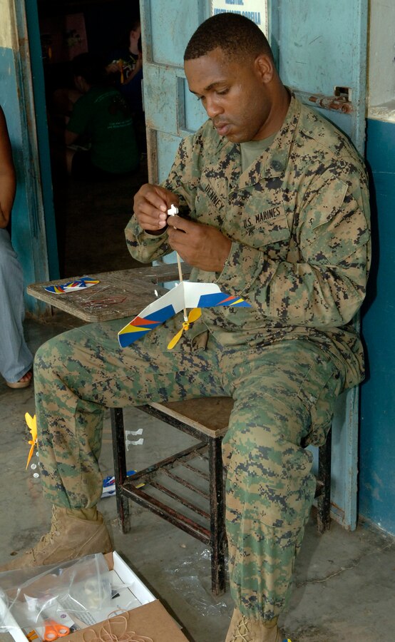 Gunnery Sgt. Howard Denney, a civil affairs Marine deployed from the 4th Civil Affairs Group, helps children assemble rubber band airplanes at the Sansonsito School July 12. (U.S. Air Force photo/Tech. Sgt. Eric Petosky)::r::::n::