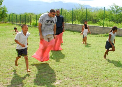 COMAYAGUA, Honduras -- Staff Sgt. Jamie Rosenthal and Tech. Sgt. Lineus Davis, both of the 612th Air Base Squadron, jump to the sack race finish line as the children of the Nuestra Señora de Guadalupe orphanage cheer them on here Friday, July 9. Other activities the 612th ABS volunteers planned for the afternoon included jump rope, soccer and tug-of-war. (U.S. Air Force photo/Tech. Sgt. Benjamin Rojek)