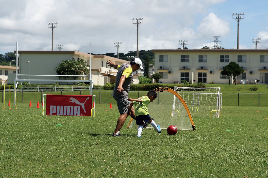 Roberto Iwashita, the Brazilian Soccer Club coach, plays a quick game of soccer with Marcos A. Orocco, 6, during soccer camp at the football field behind Zukeran Elementary School on Camp Foster.