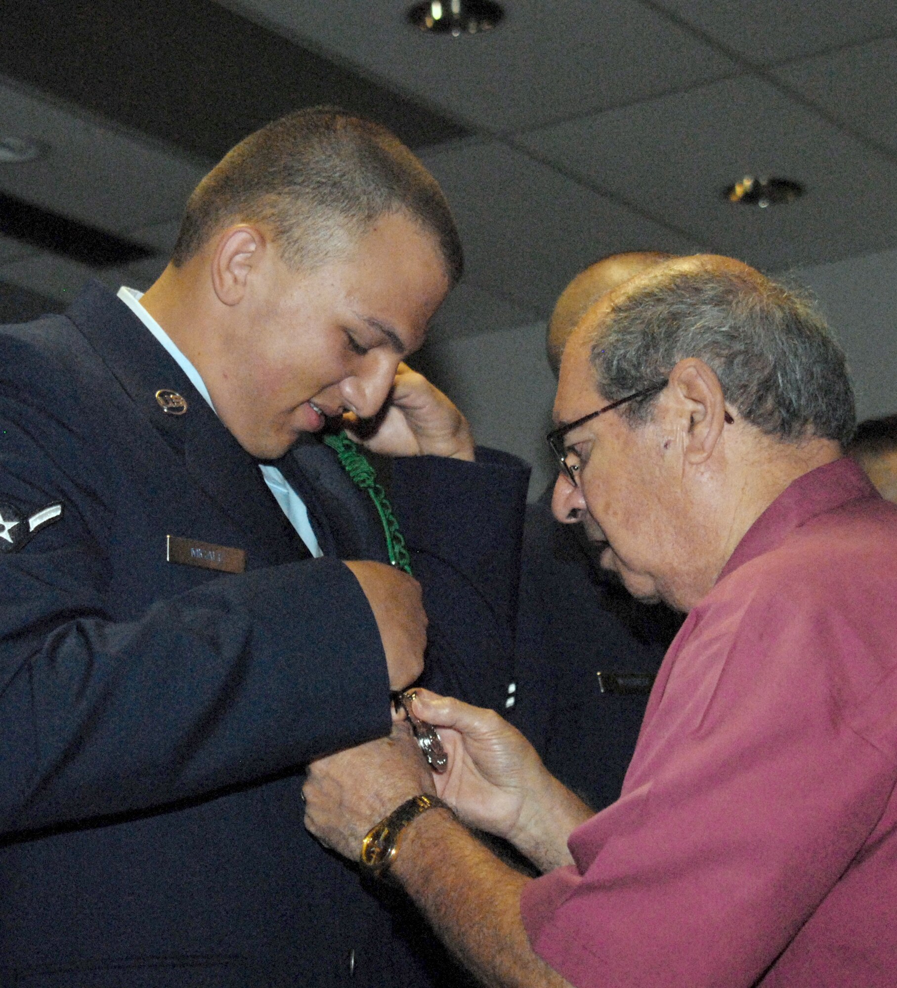 Airman 1st Class Laurence Micale watches as his grandfather, retired Col. Peter Micale III, pins on his new fire protection badge during the graduation ceremony July 1, 2010, at Goodfellow Air Force Base, Texas. Airman Micale is a third generation Air Force member with family ties going back to the start of the Air Force. (U.S. Air Force photo/Connie Hempel)