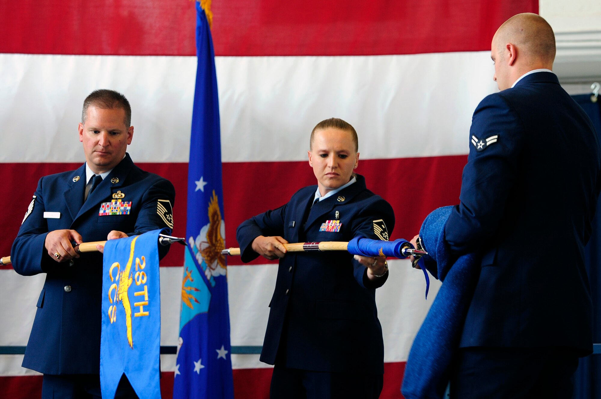 ELLSWORTH AIR FORCE BASE S.D. – (From left) Master Sgt. Philip Csornok, 28th Comptroller and Contracting Squadron first sergeant, furls the 28 CCS guidon as Master Sgt. Tina McFadden, 28th Comptroller Squadron first sergeant, unfurls the 28 CPTS guidon with the help of Airman 1st Class Joshua Ingram 28 CPTS financial analyzer, July 12.  The 28 CCS was deactivated and divided into the 28th Comptroller Squadron and the 28th Contracting Squadron. (U.S. Air Force photo/Staff Sgt. Marc I. Lane)